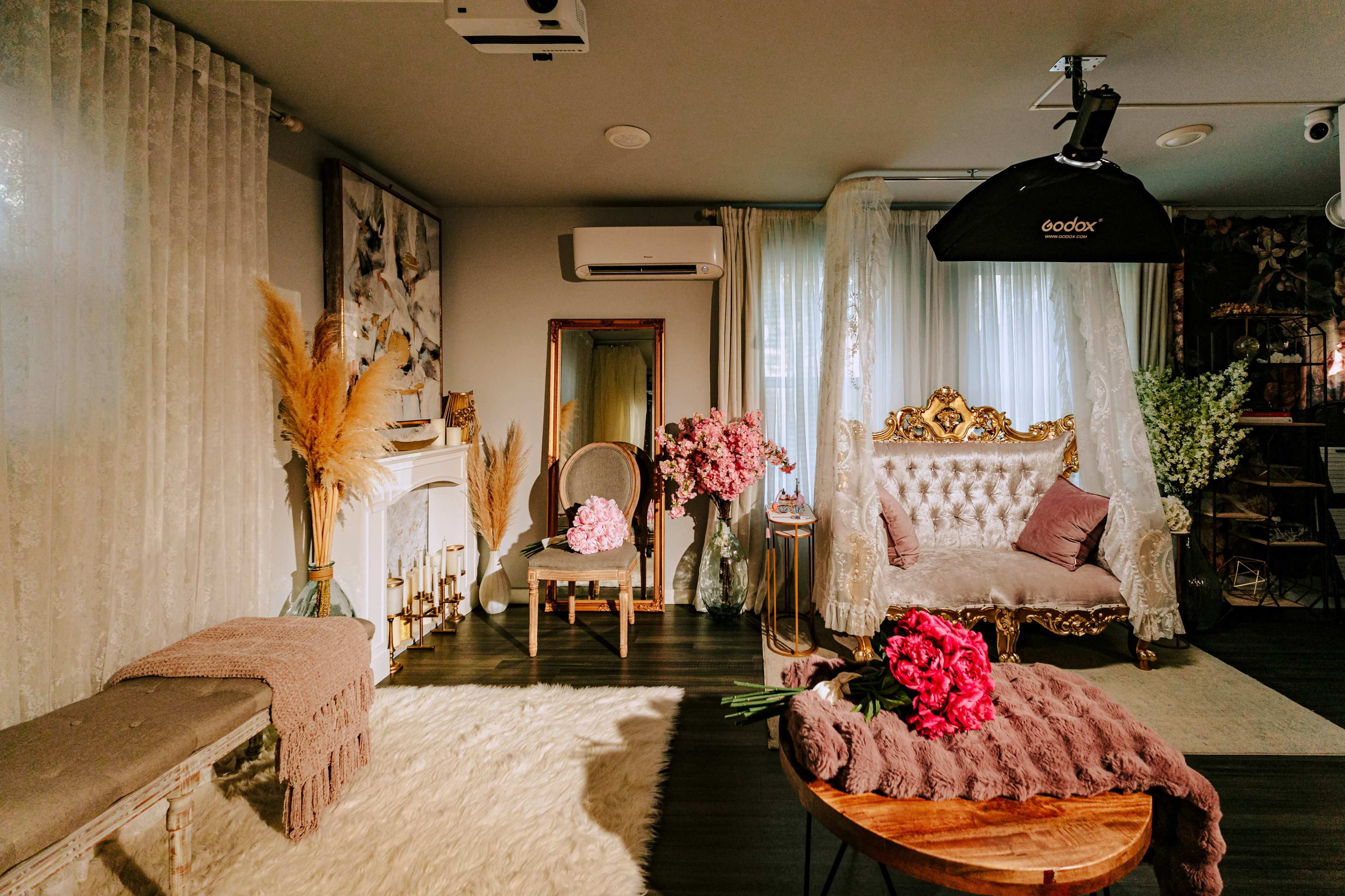 The image shows a styled interior room featuring a vintage couch with floral decor, an ornate mirror, and soft furnishings.