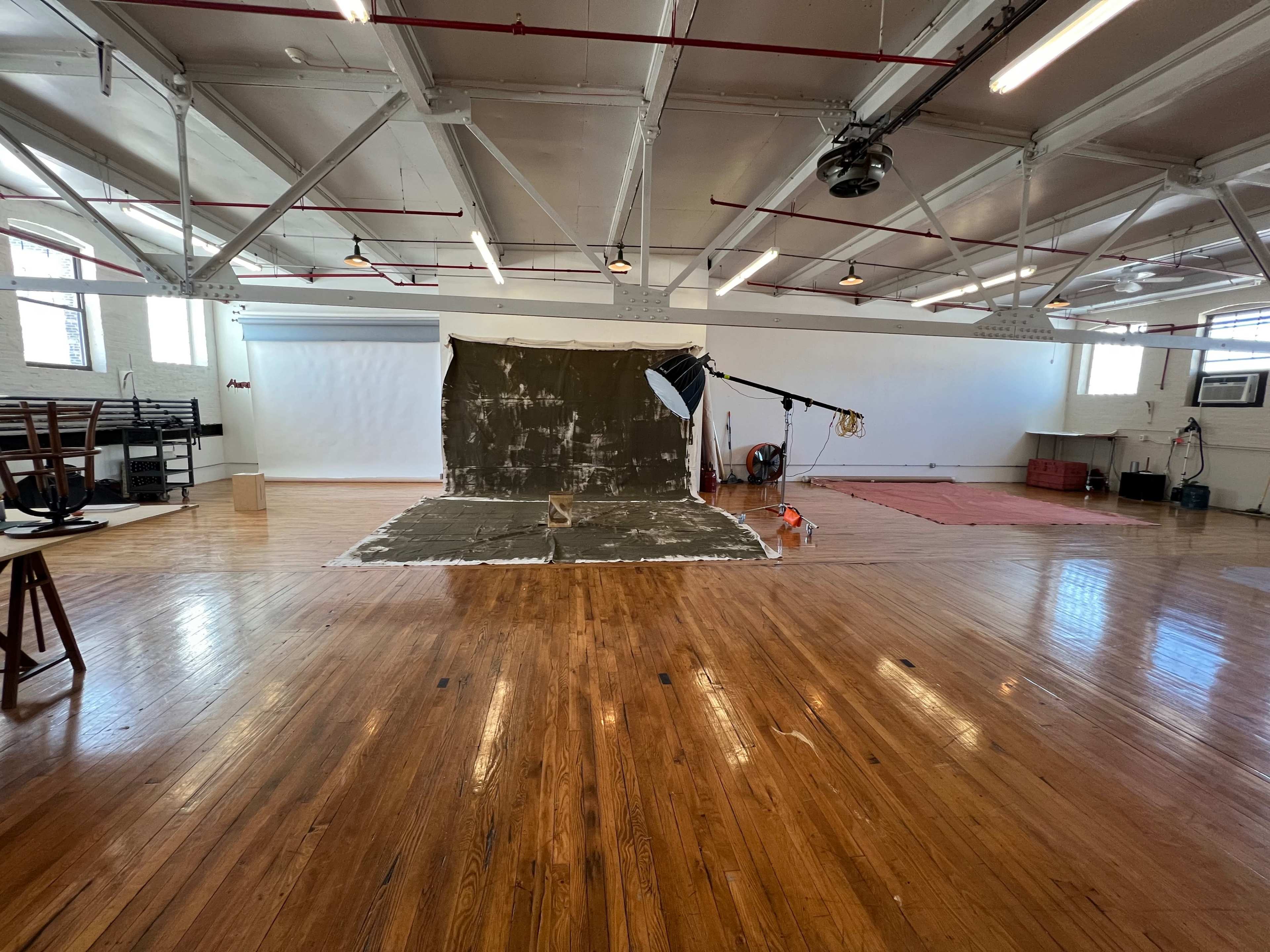 An empty photography studio features wooden floors, a backdrop, lighting equipment, and various materials arranged around the space.