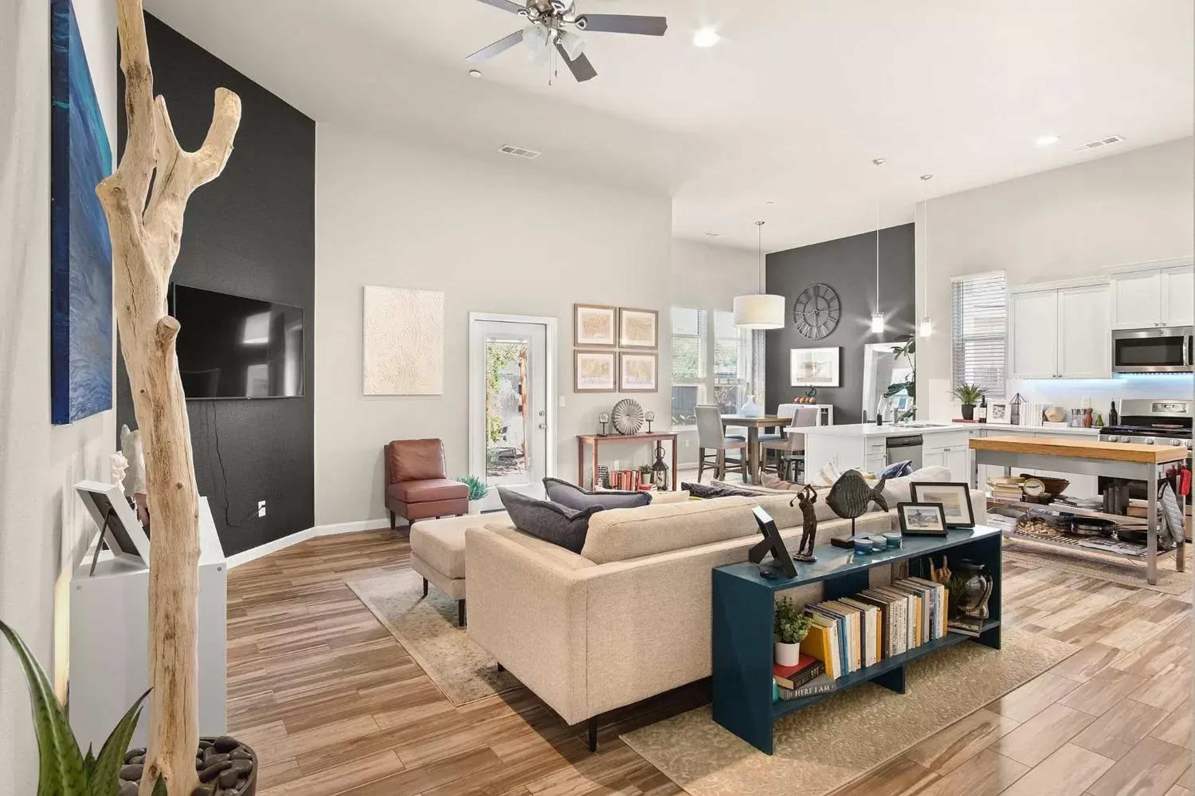 A modern living room with a sectional couch, a coffee table holding books, and an open kitchen area in the background.