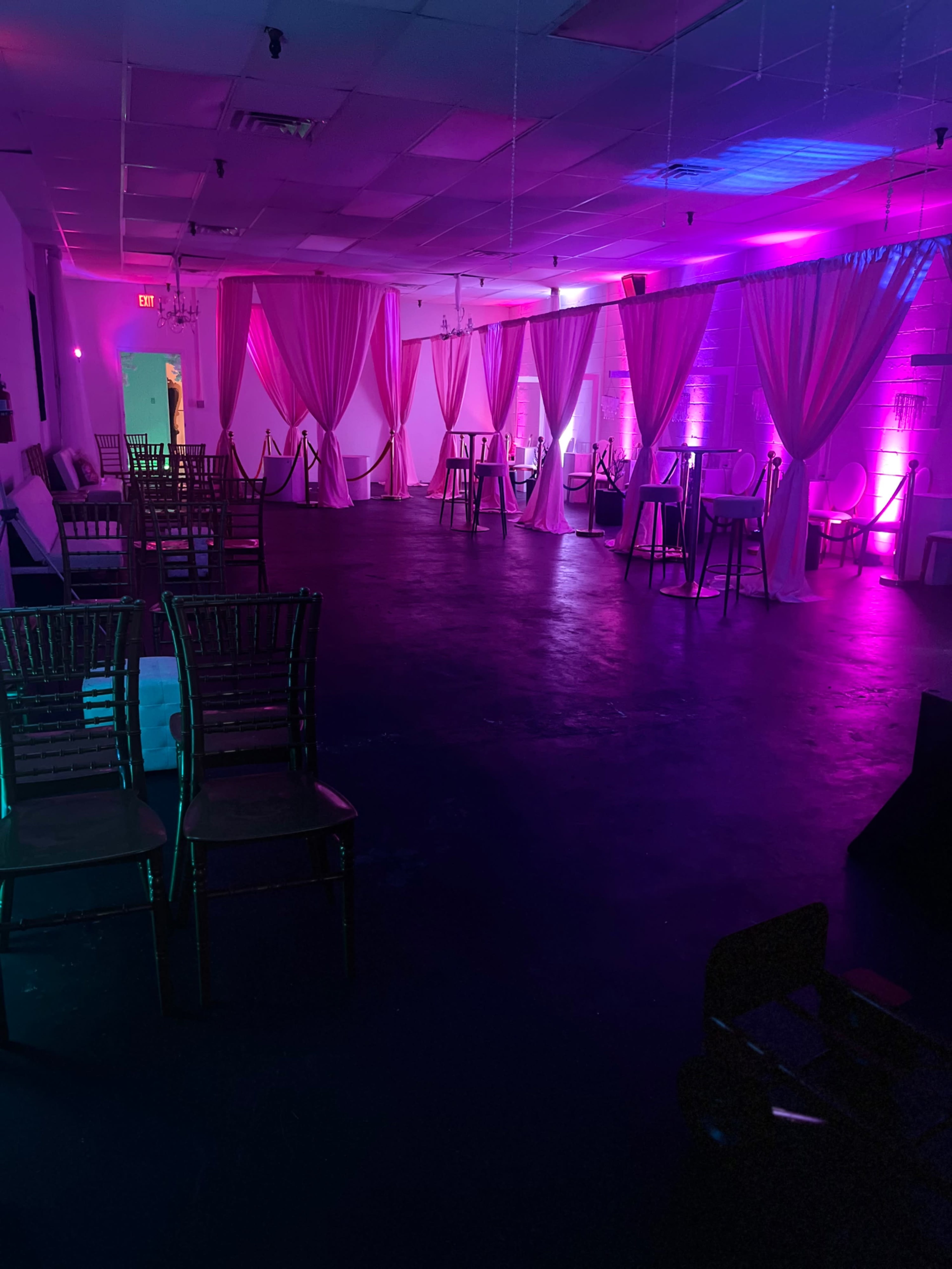 An event space with draped fabric, chairs arranged around the area, and pink and purple lighting.