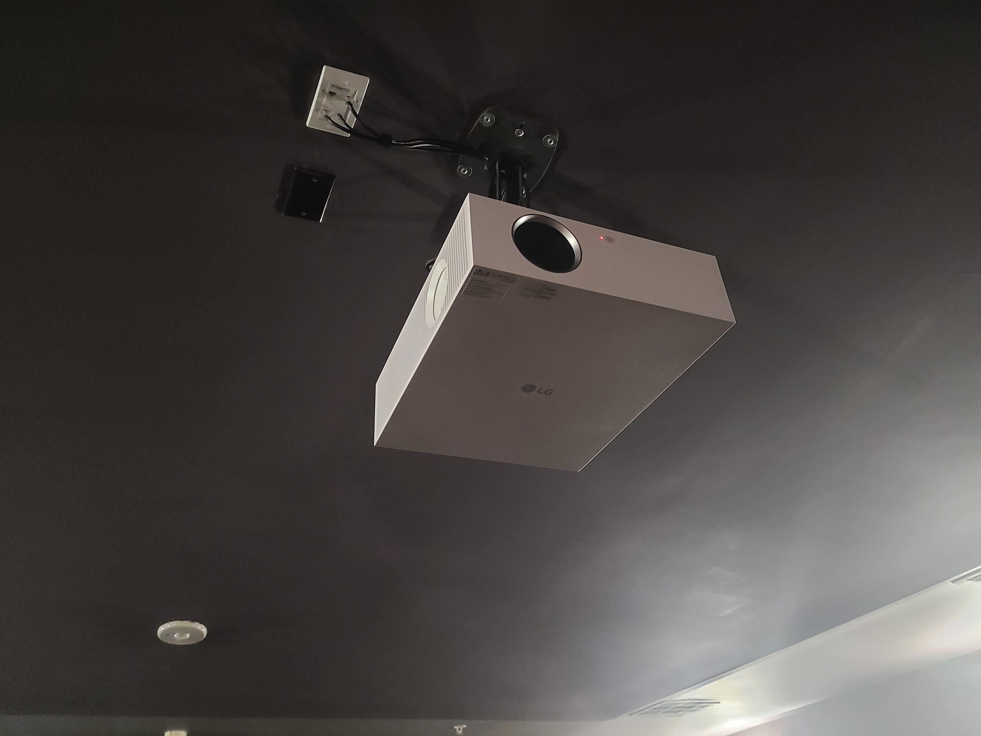 A white LG projector mounted on a dark ceiling.