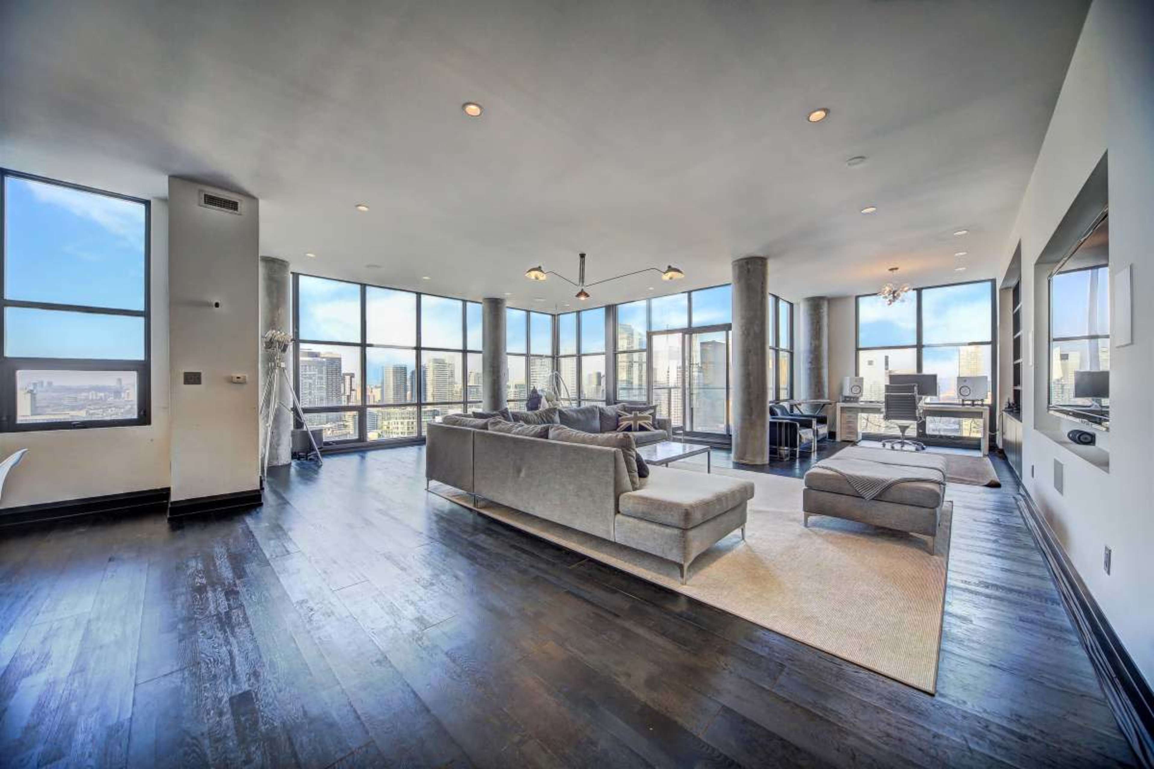 The image shows a modern apartment living room with large windows offering a view of a city skyline.