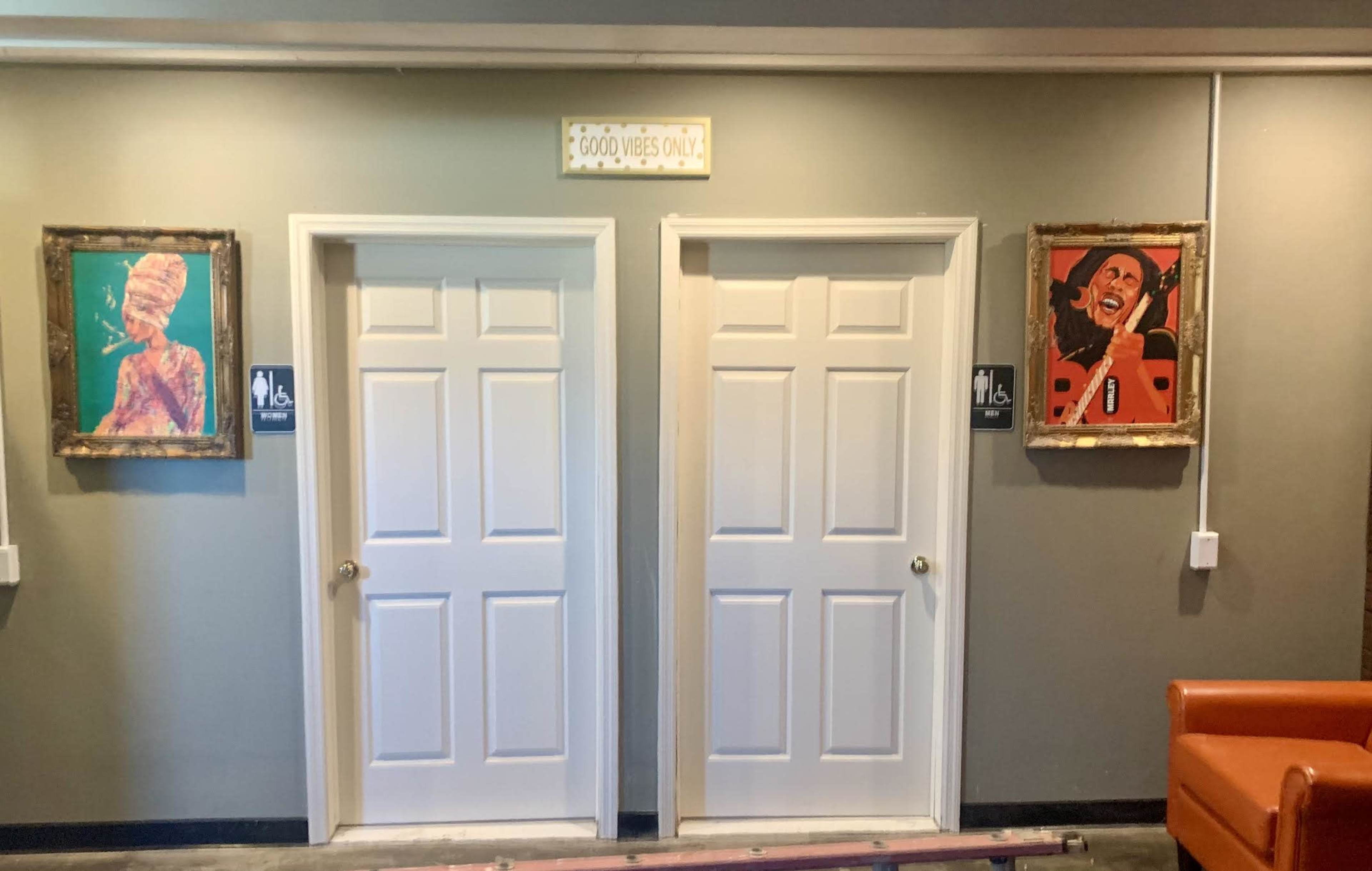 The image shows a hallway with two white doors flanked by paintings and a sign above that reads "GOOD VIBES ONLY."
