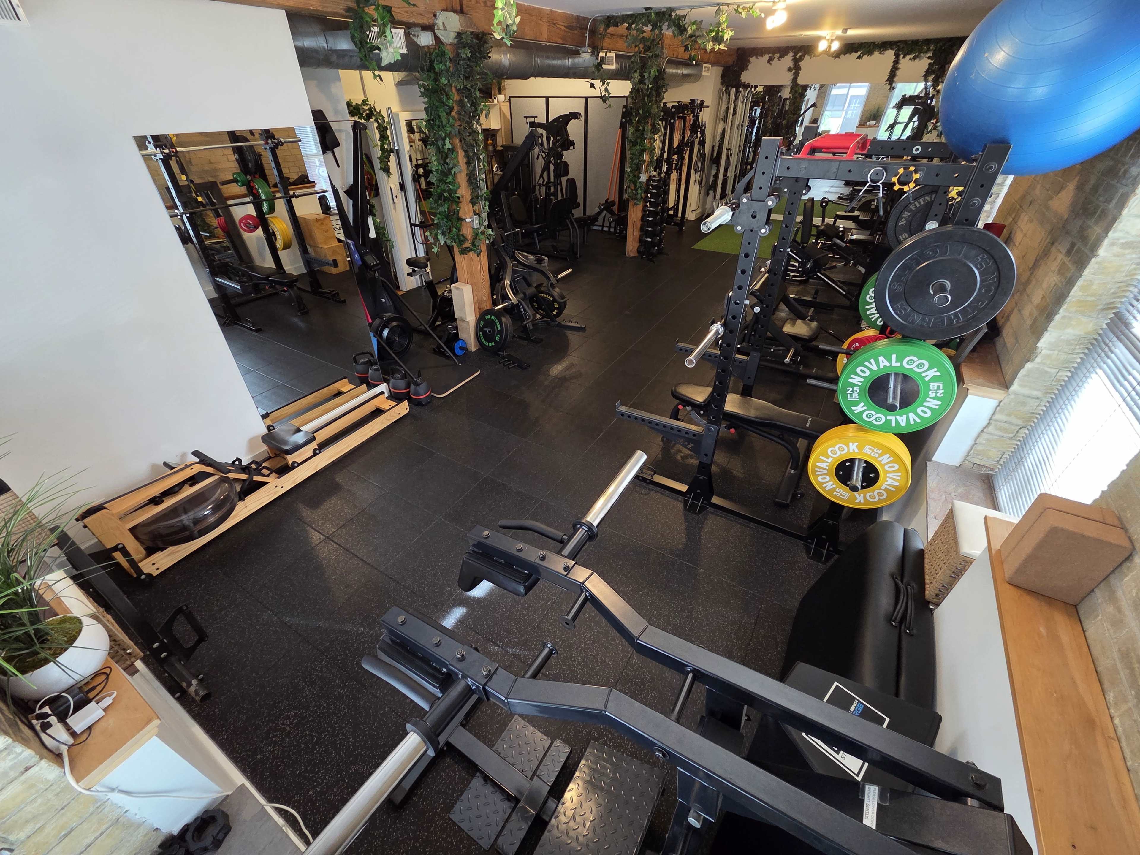 The image shows a spacious gym equipped with various fitness machines, weights, and exercise equipment, arranged in an organized manner.