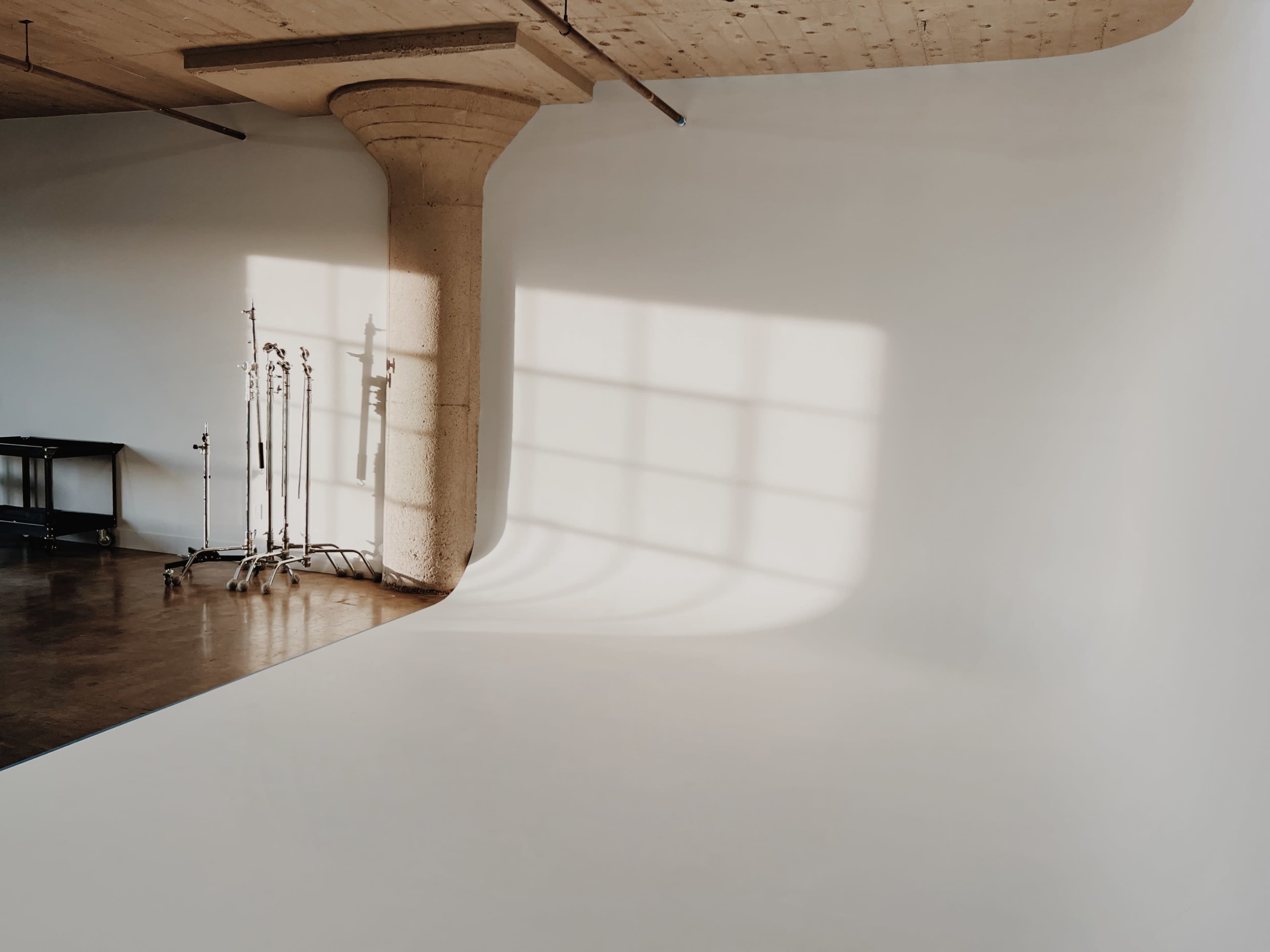A minimalistic photography studio with a curved white backdrop and a concrete support pillar, illuminated by soft natural light.