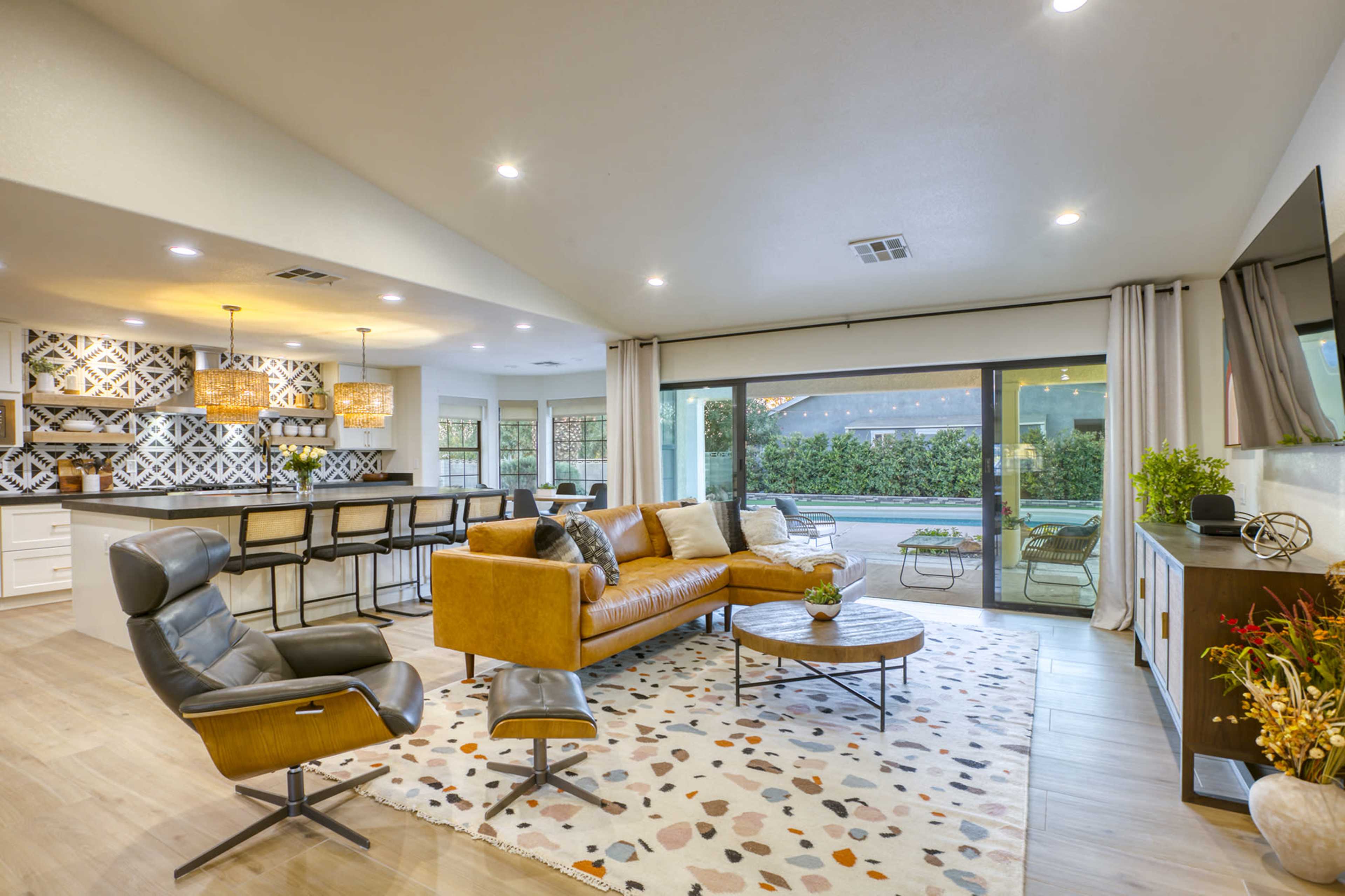 A modern living room features a leather sofa, a coffee table, and an open view to a patio through large sliding glass doors.