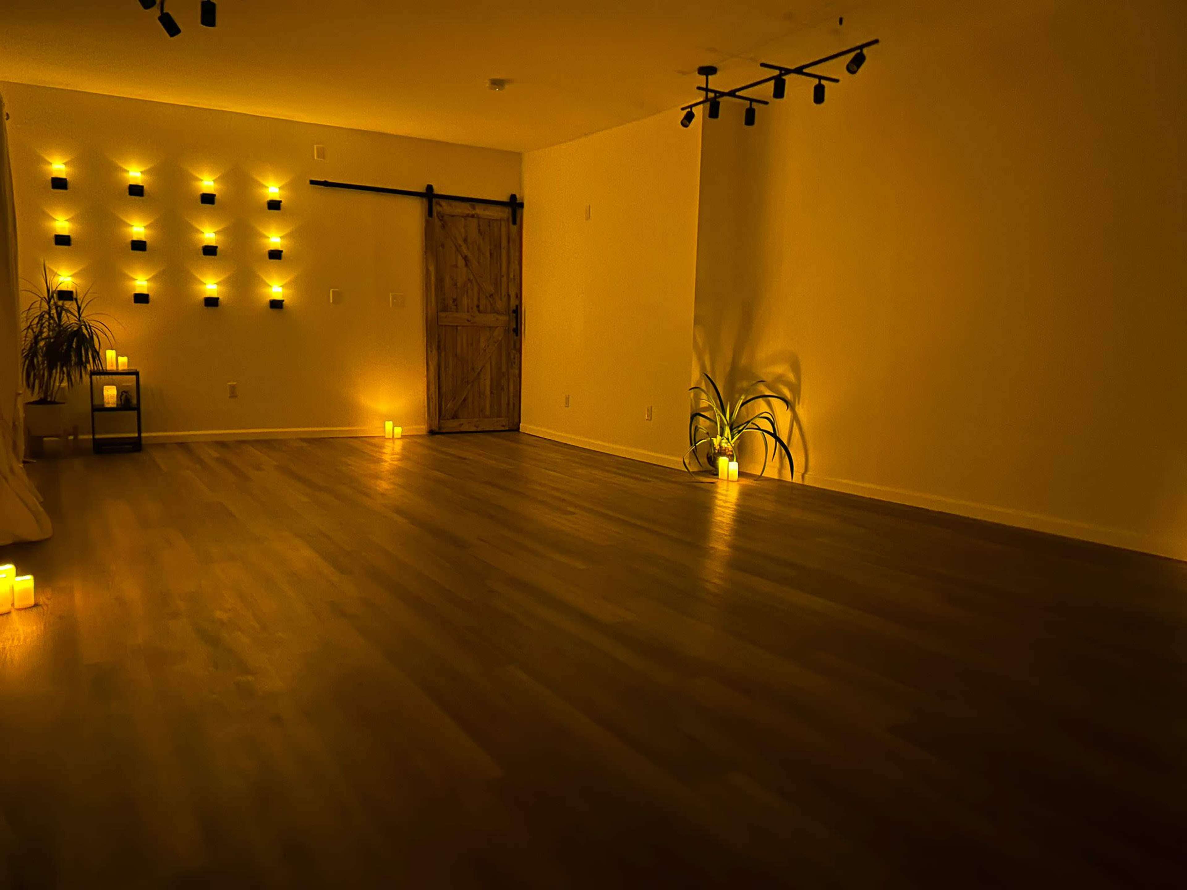 A softly lit, minimalist room with candles on the floor and wall-mounted plants, featuring a wooden sliding door.