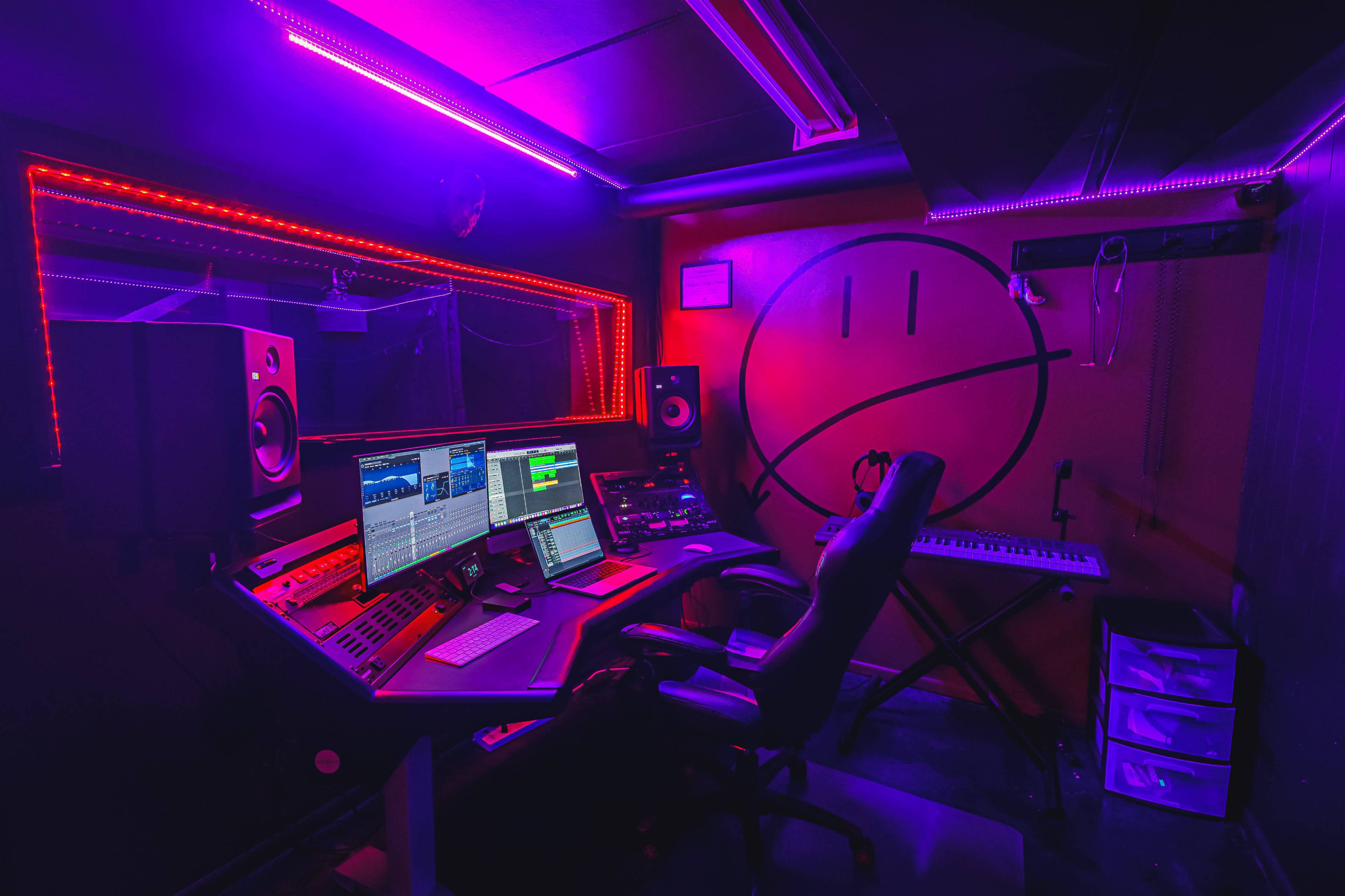 A dimly lit music studio featuring a control console, computer monitors, and colorful LED lights illuminating the room.