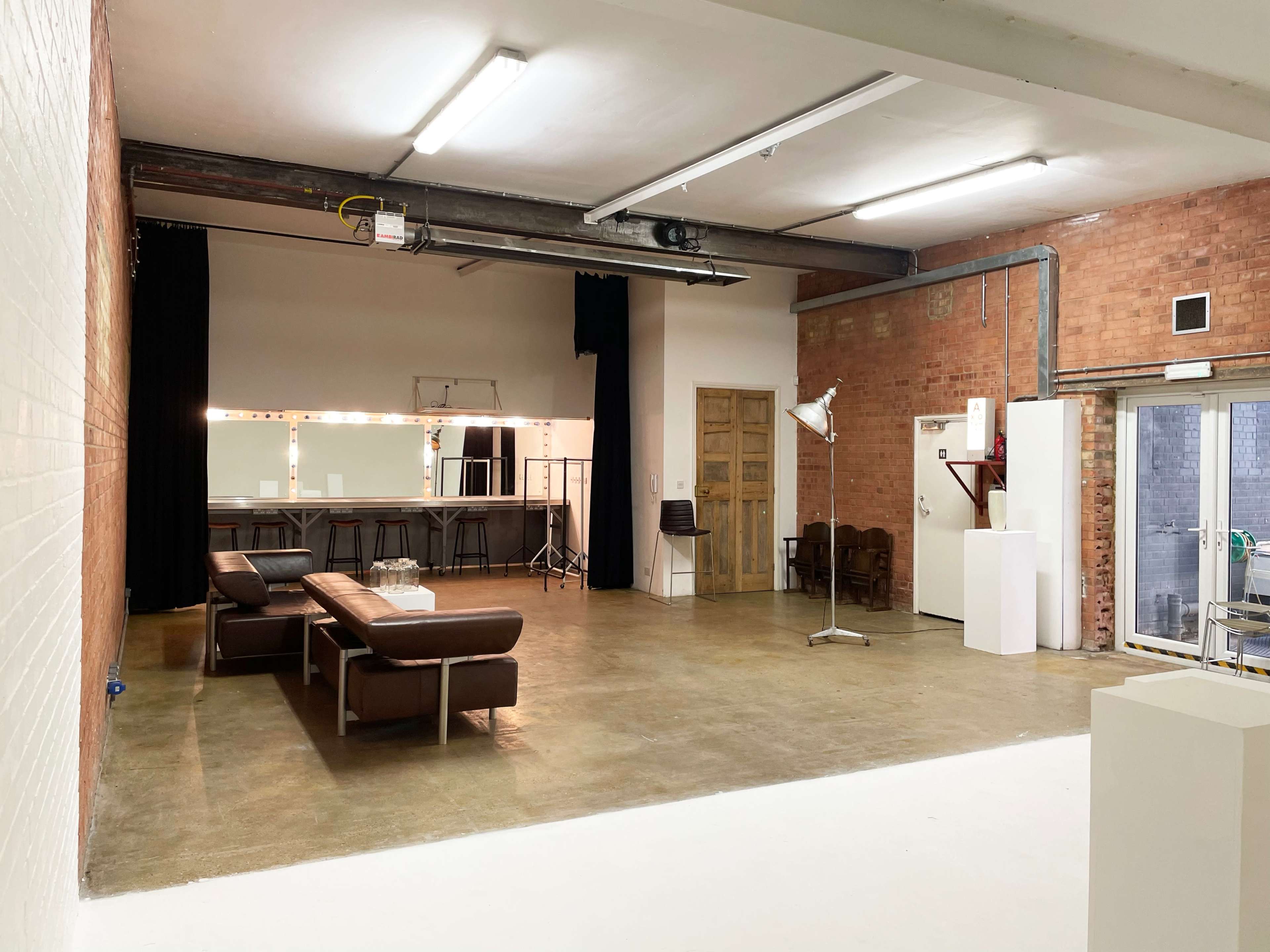 A spacious, well-lit studio with a seating area, mirrors, and equipment setups against exposed brick walls.