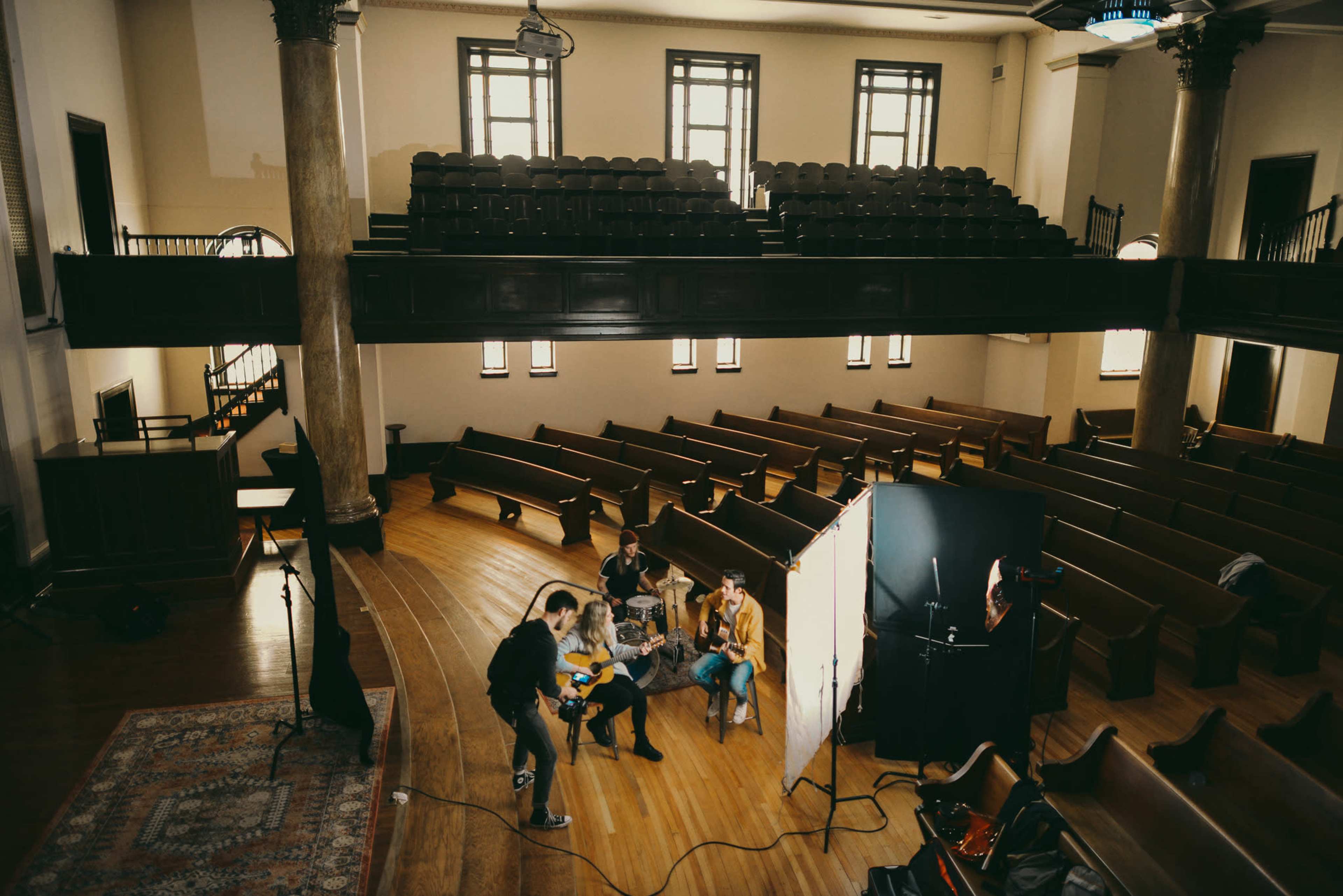 A group of people is gathered for a photo shoot in an empty auditorium with wooden pews.
