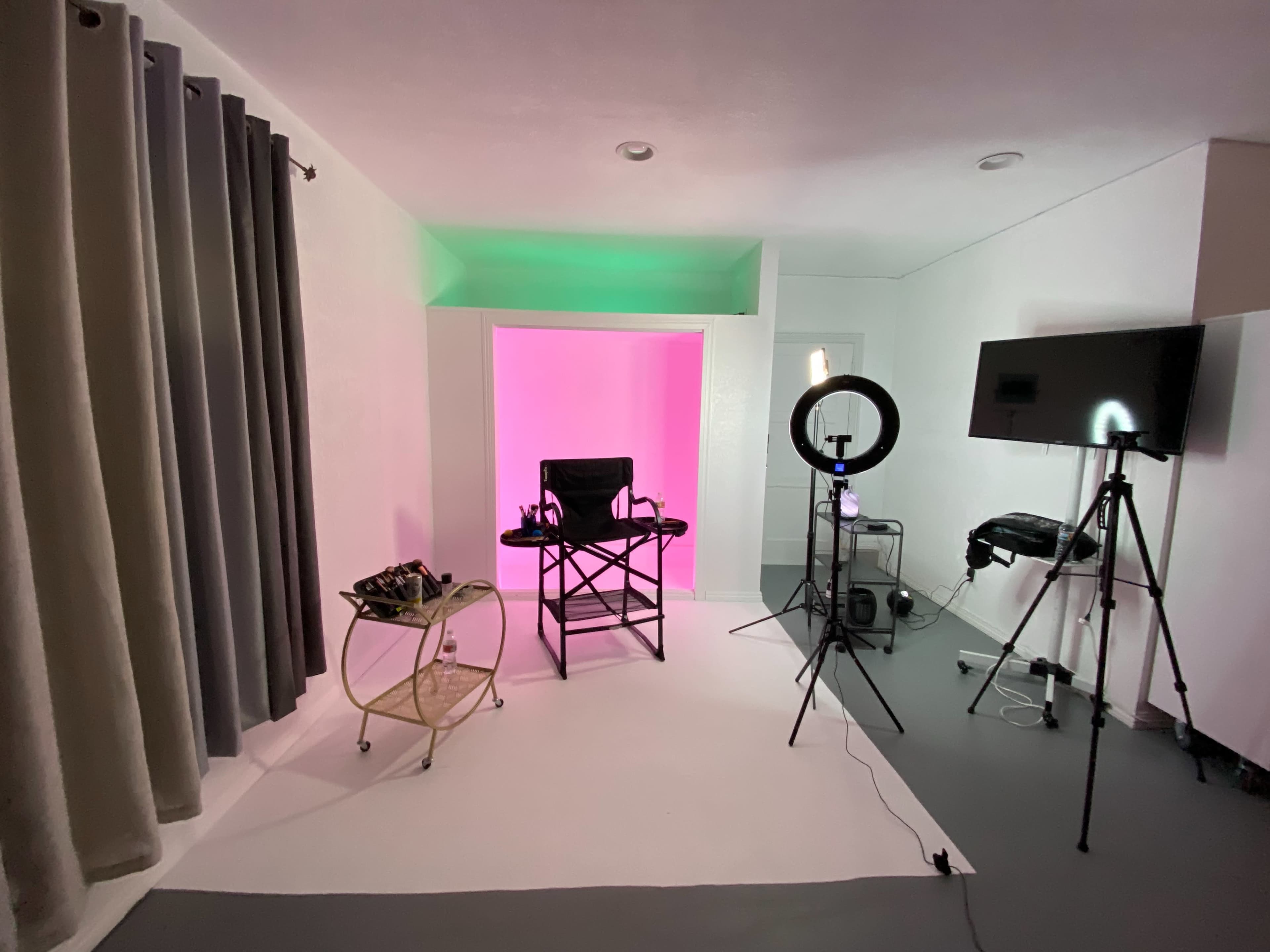A studio space with a makeup chair, lighting equipment, and a backdrop featuring pink lighting.