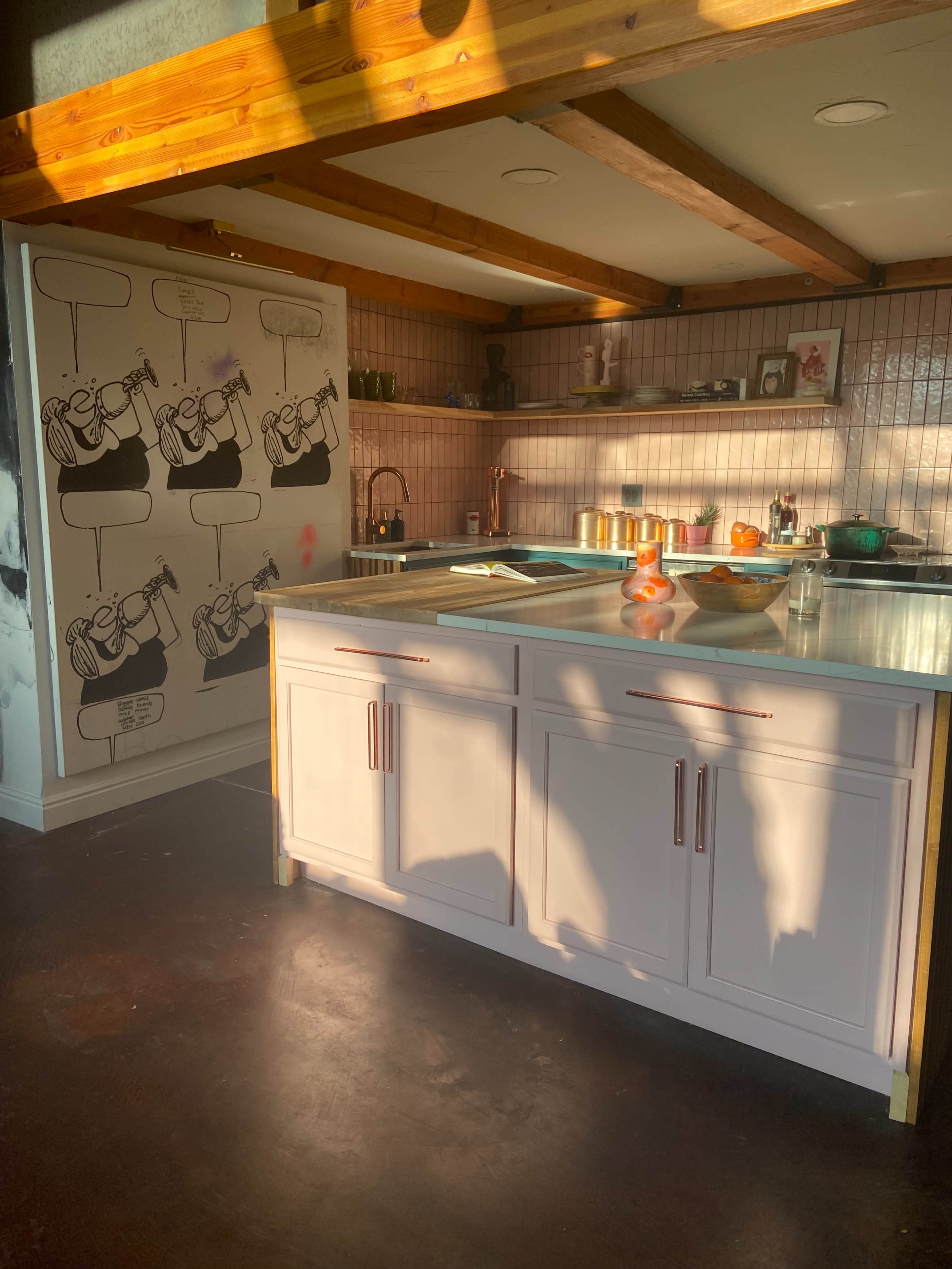 A modern kitchen with a central island, wooden beams on the ceiling, and a colorful mural on the refrigerator.