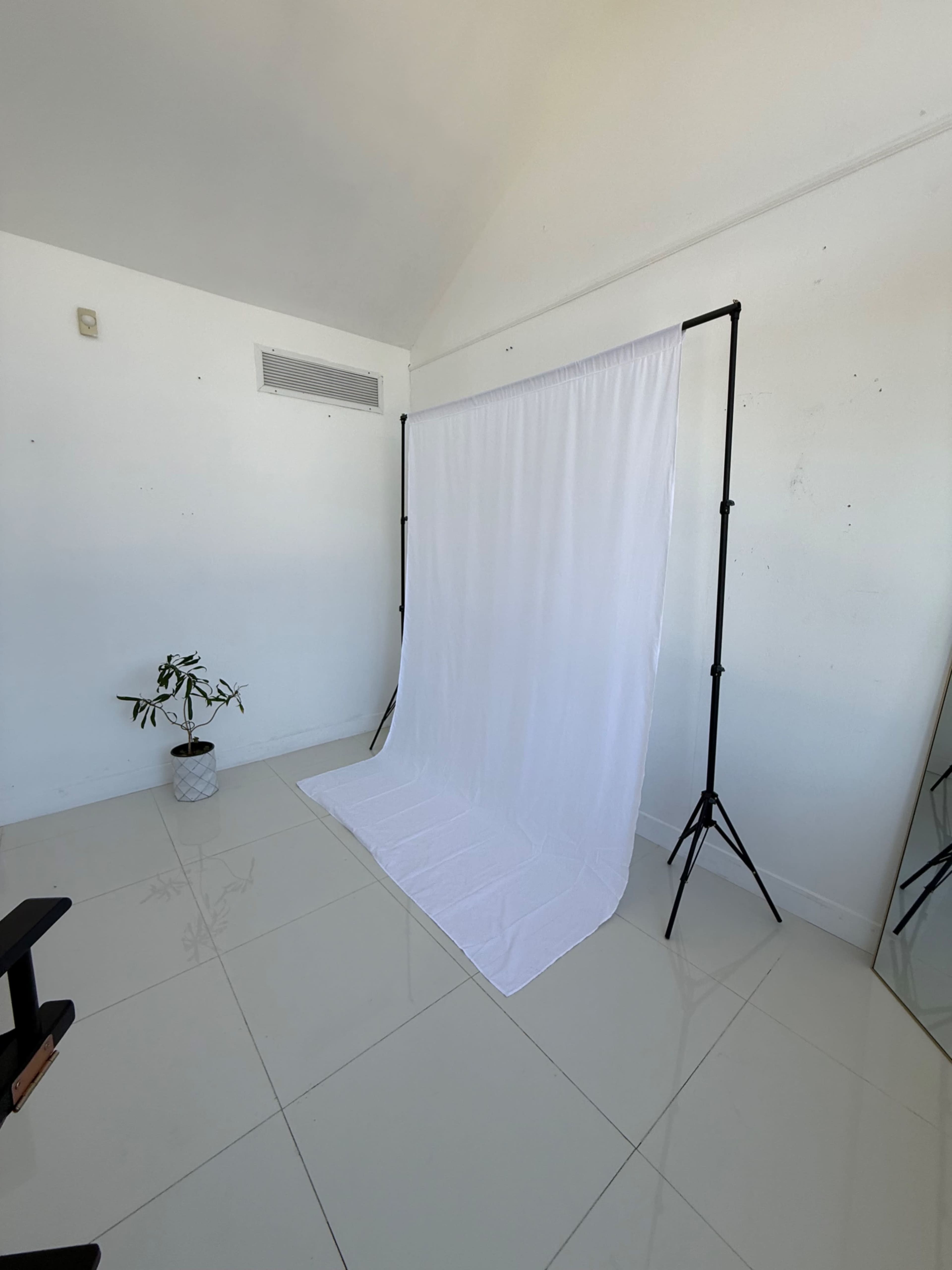 The image shows a photography setup with a white backdrop on a black stand in a spacious, brightly lit room with tiled flooring.