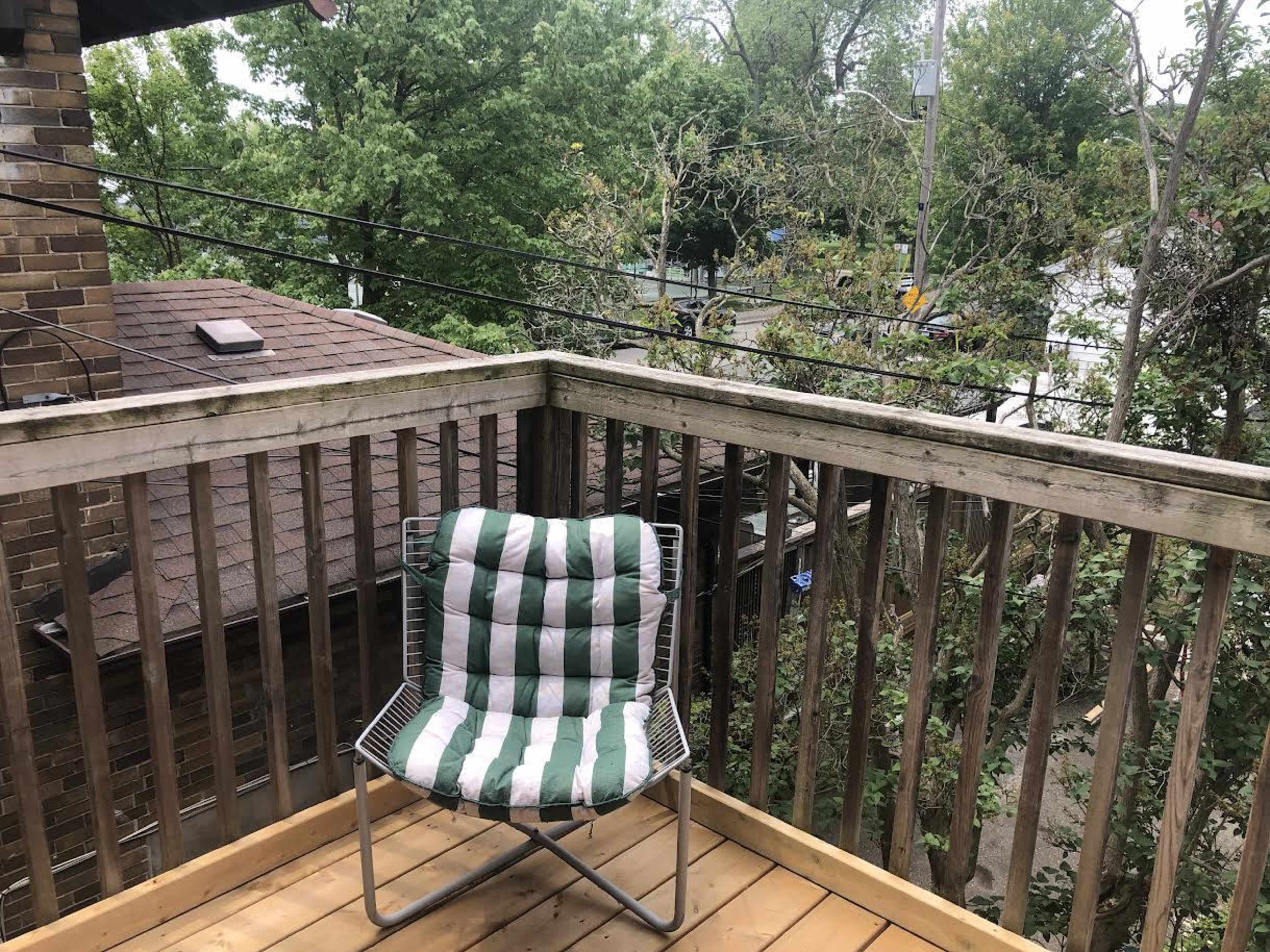 The image shows a balcony with a striped chair overlooking trees and a street.