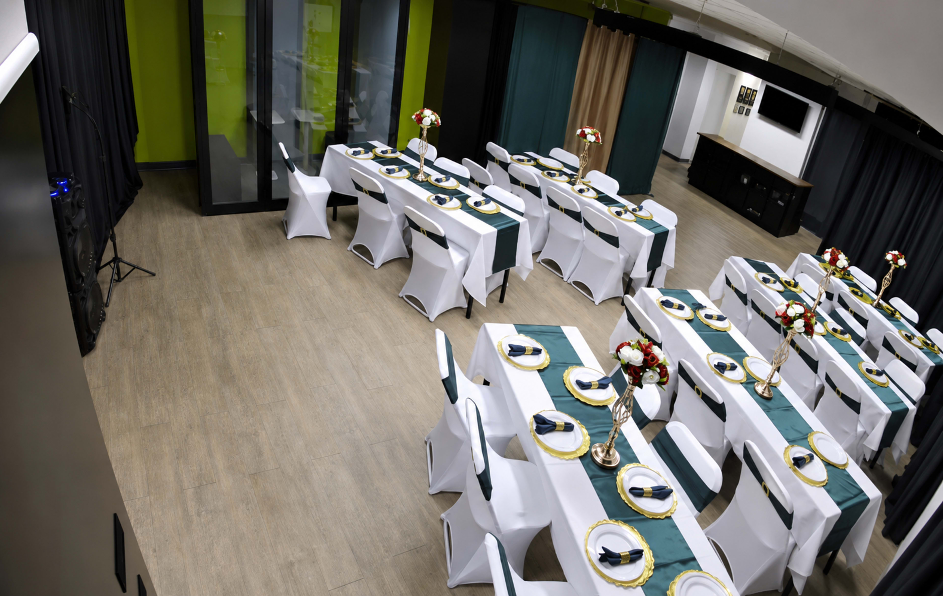 The image shows a banquet hall set up with several tables covered in white linens and teal accents, arranged in a U-shape, with floral centerpieces and tableware neatly placed.