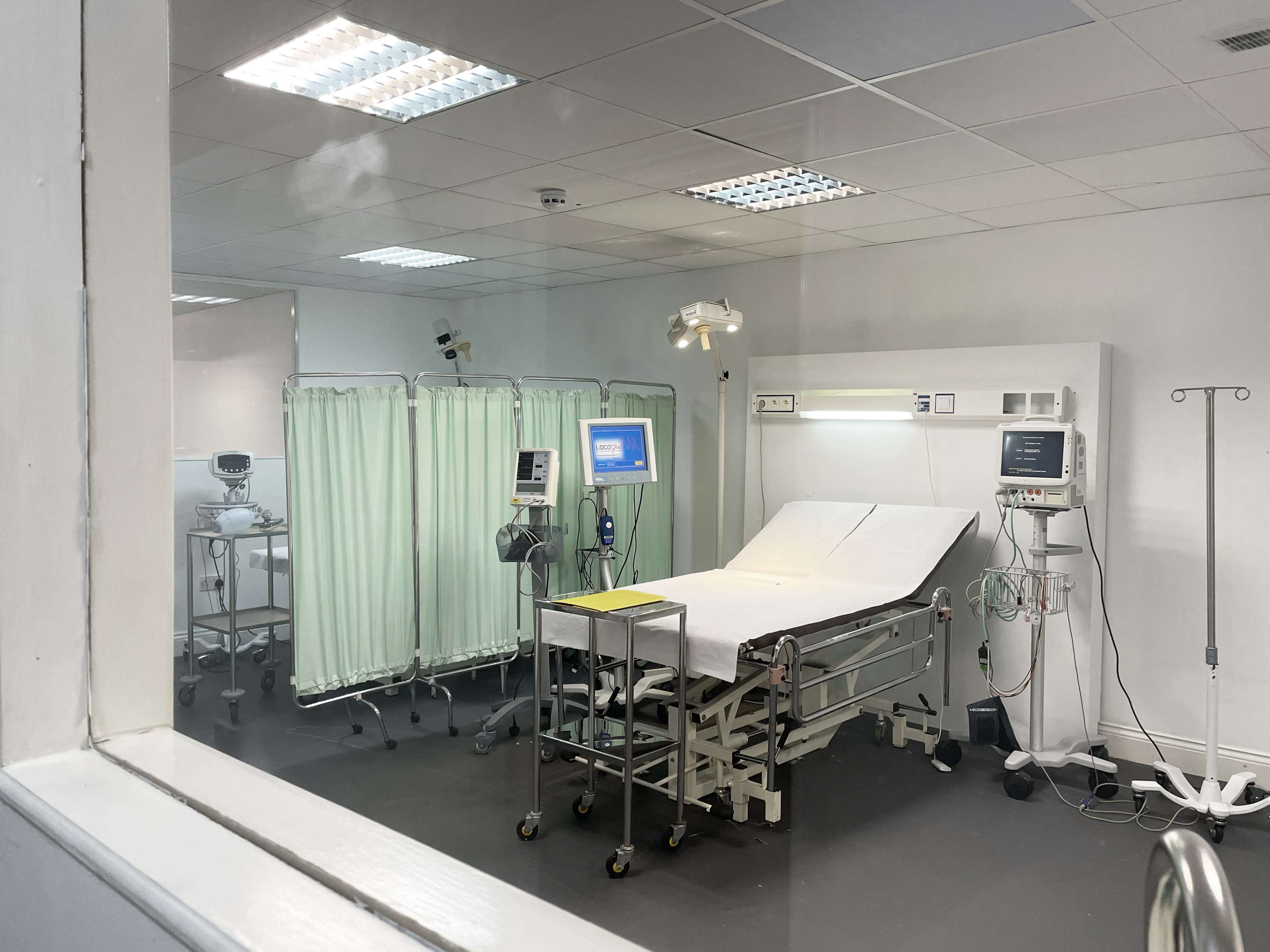 A hospital examination room with a bed, medical equipment, and privacy curtains.