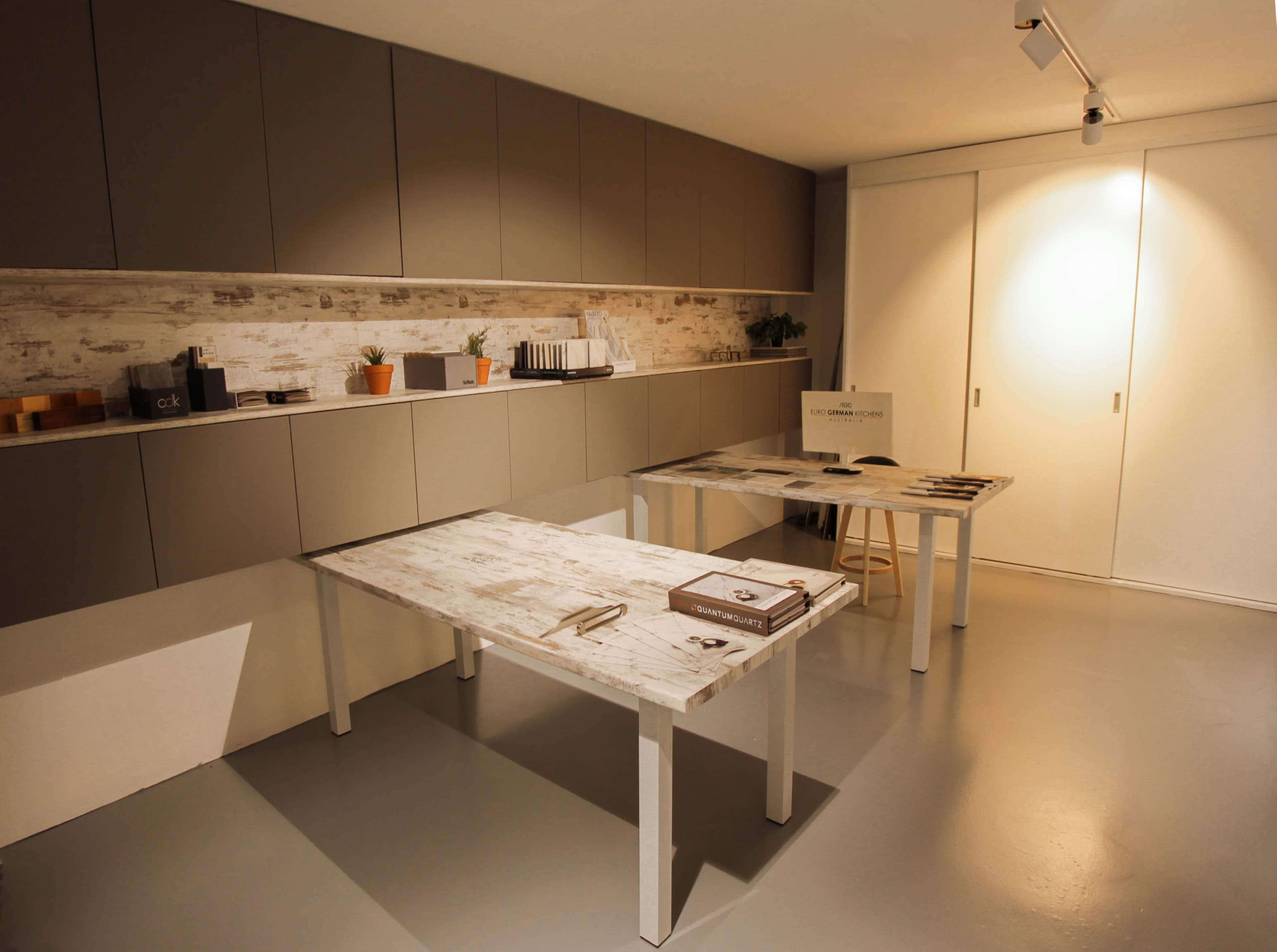 The image shows a modern, minimalist dining area with two tables and a wall-mounted cabinet featuring potted plants.