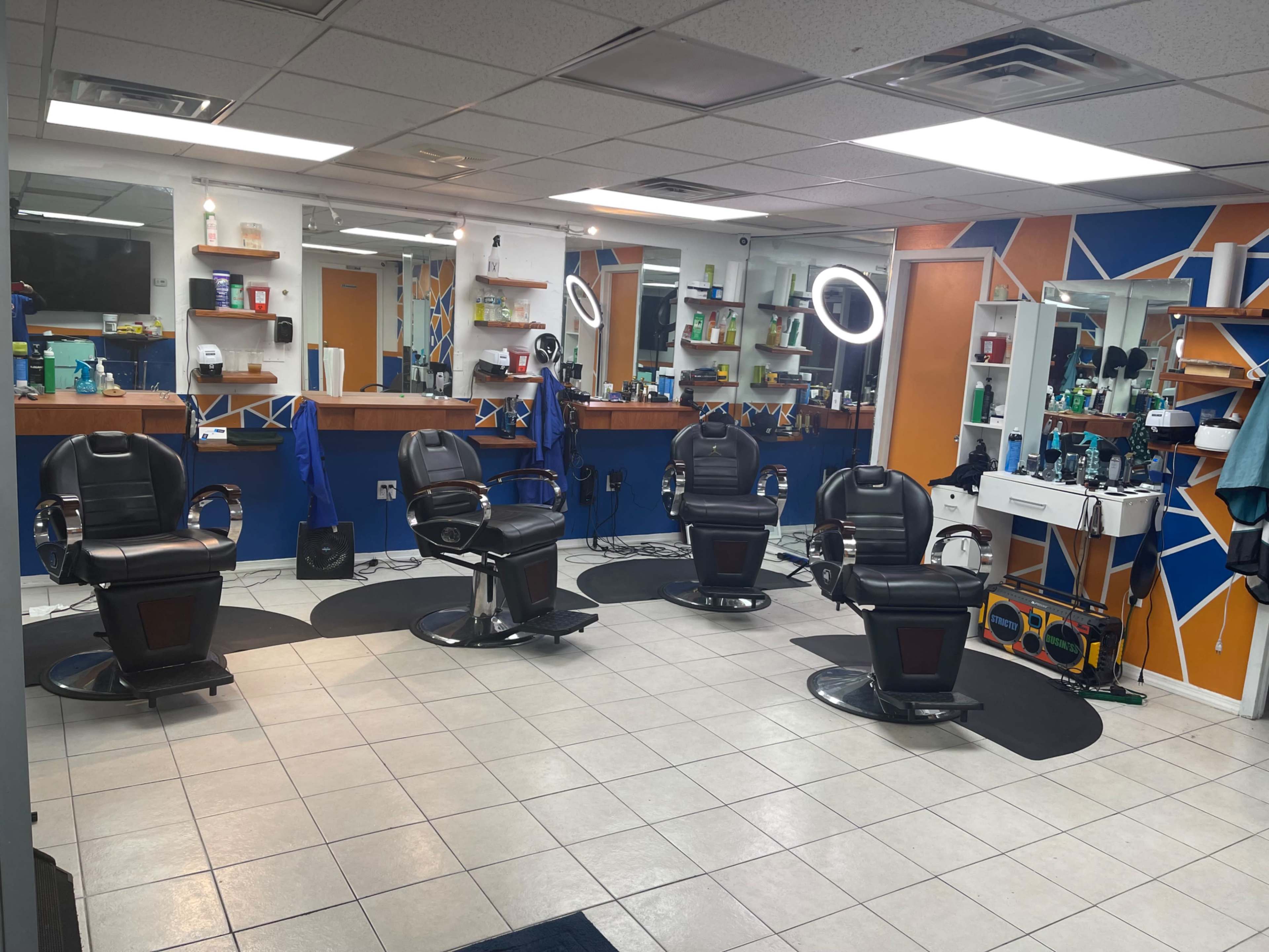The image shows a barbershop with several barber chairs arranged in a circular layout, surrounded by mirrors and grooming supplies on the walls.