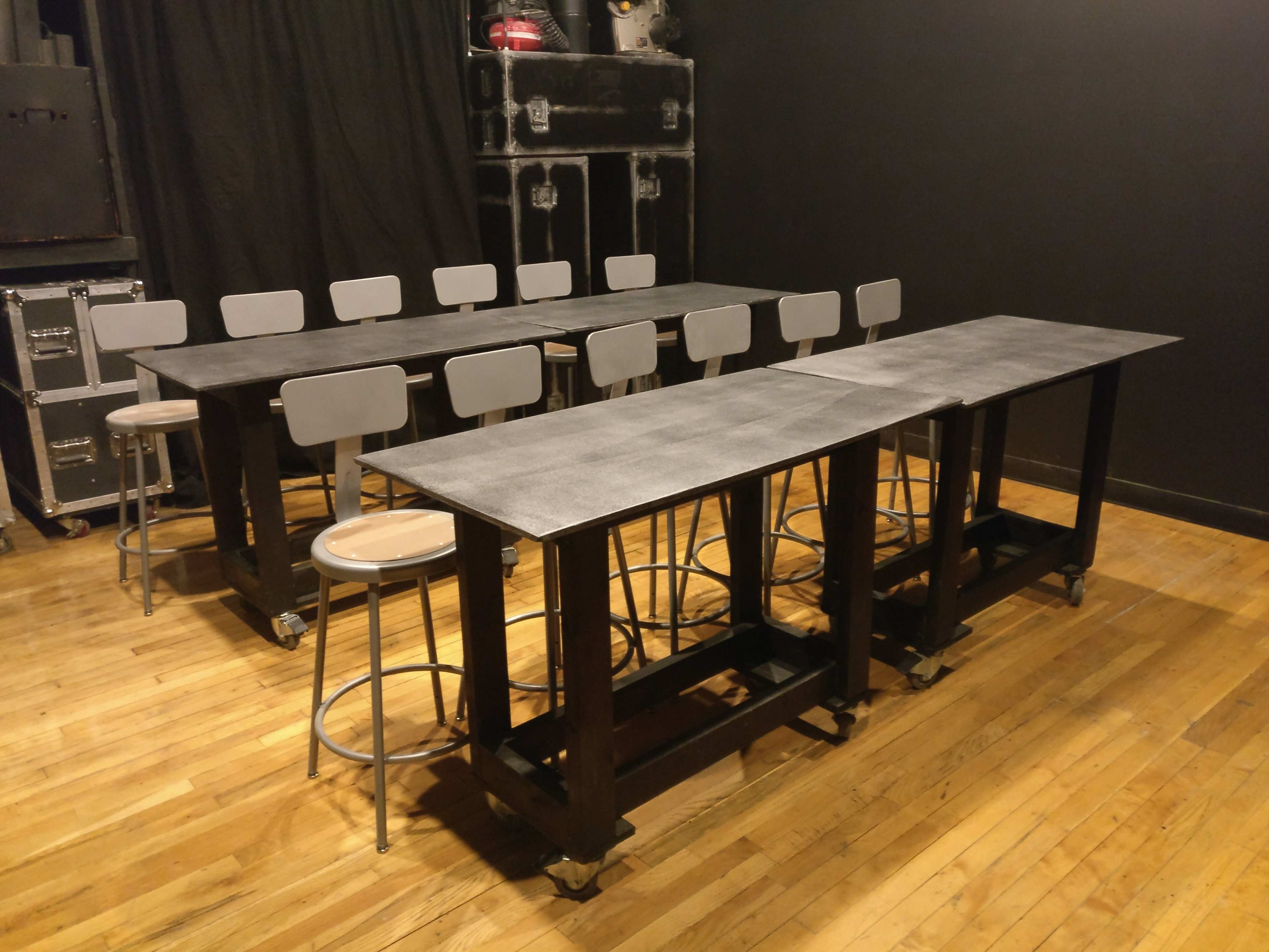 Two rectangular tables with a row of stools behind them in a dimly lit room.