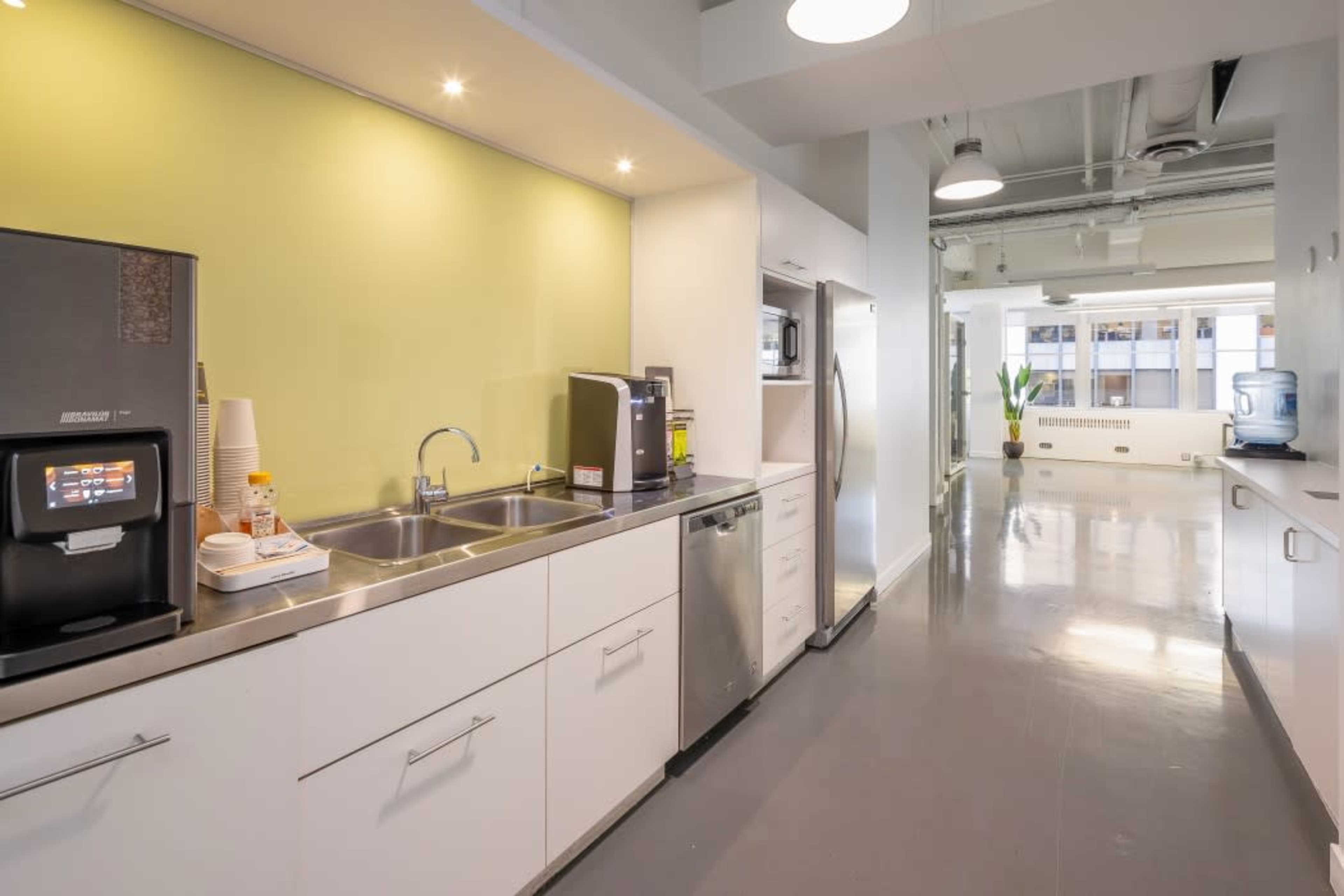 A modern kitchen area featuring stainless steel appliances, a double sink, and a countertop with a coffee machine against a green accent wall.