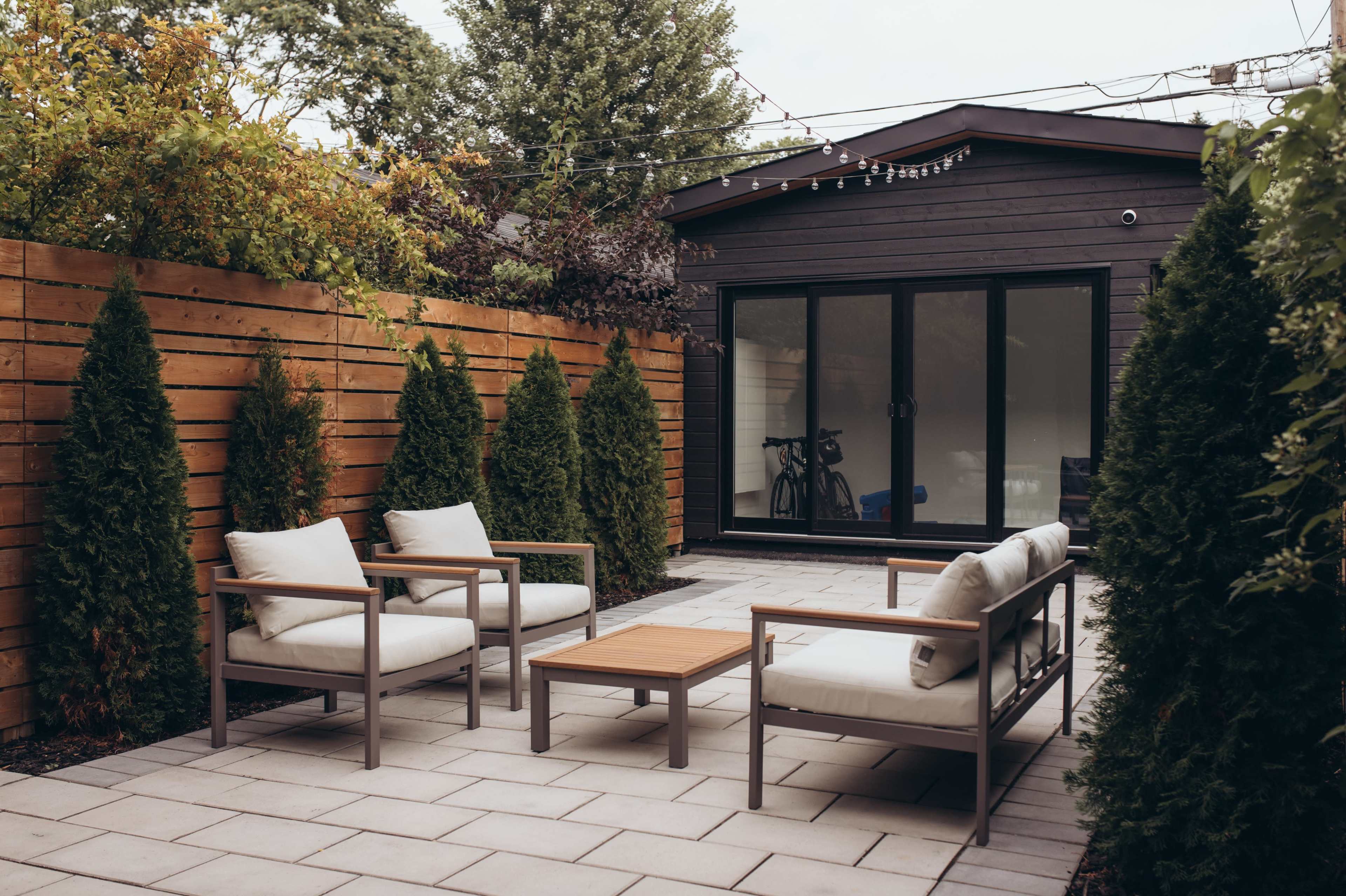 A modern patio area with two chairs and a table surrounded by tall hedges and a building in the background.
