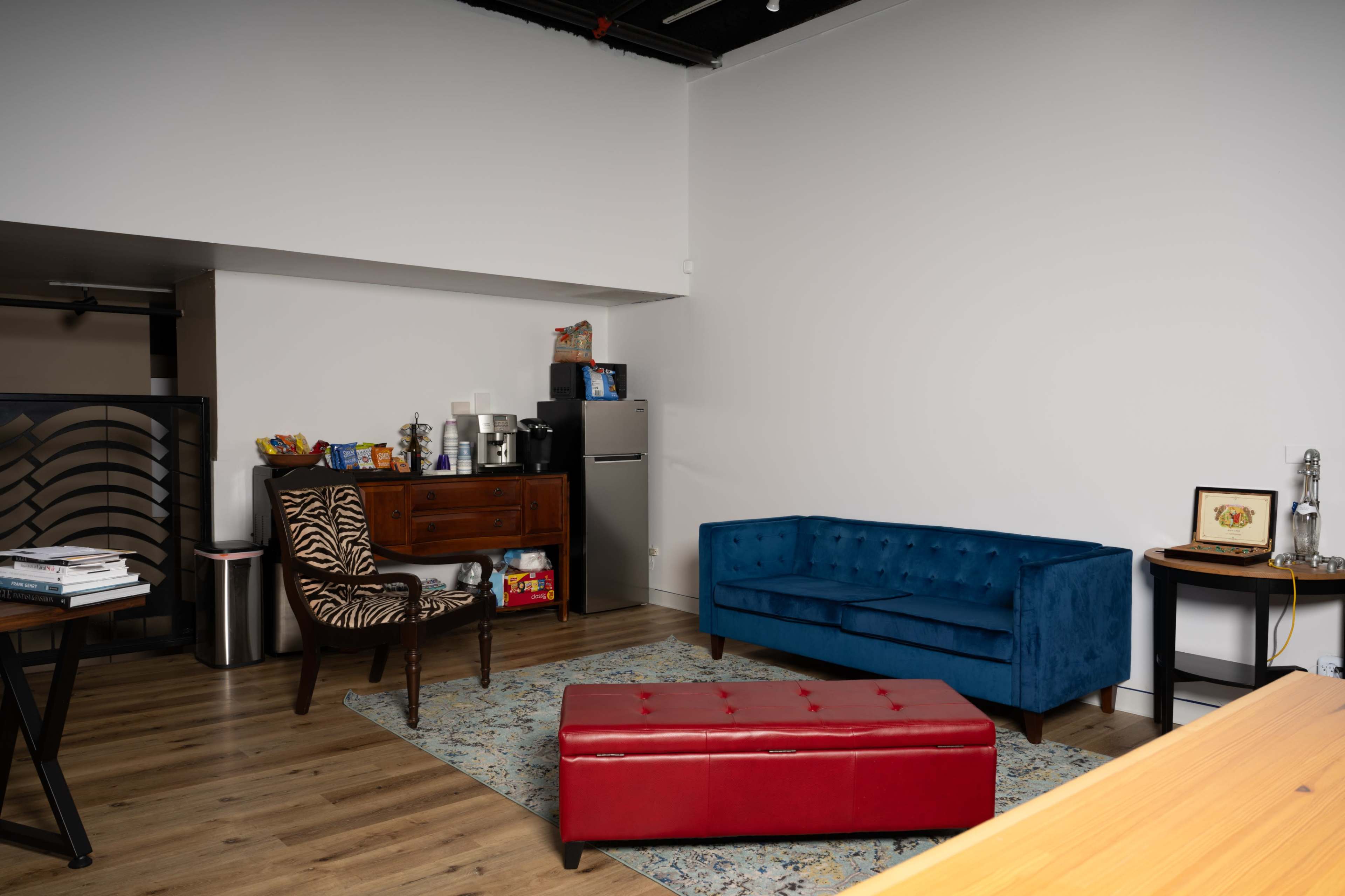A modern, minimalistic living space featuring a blue sofa, a red ottoman, a zebra-patterned chair, and a rustic wooden cabinet.