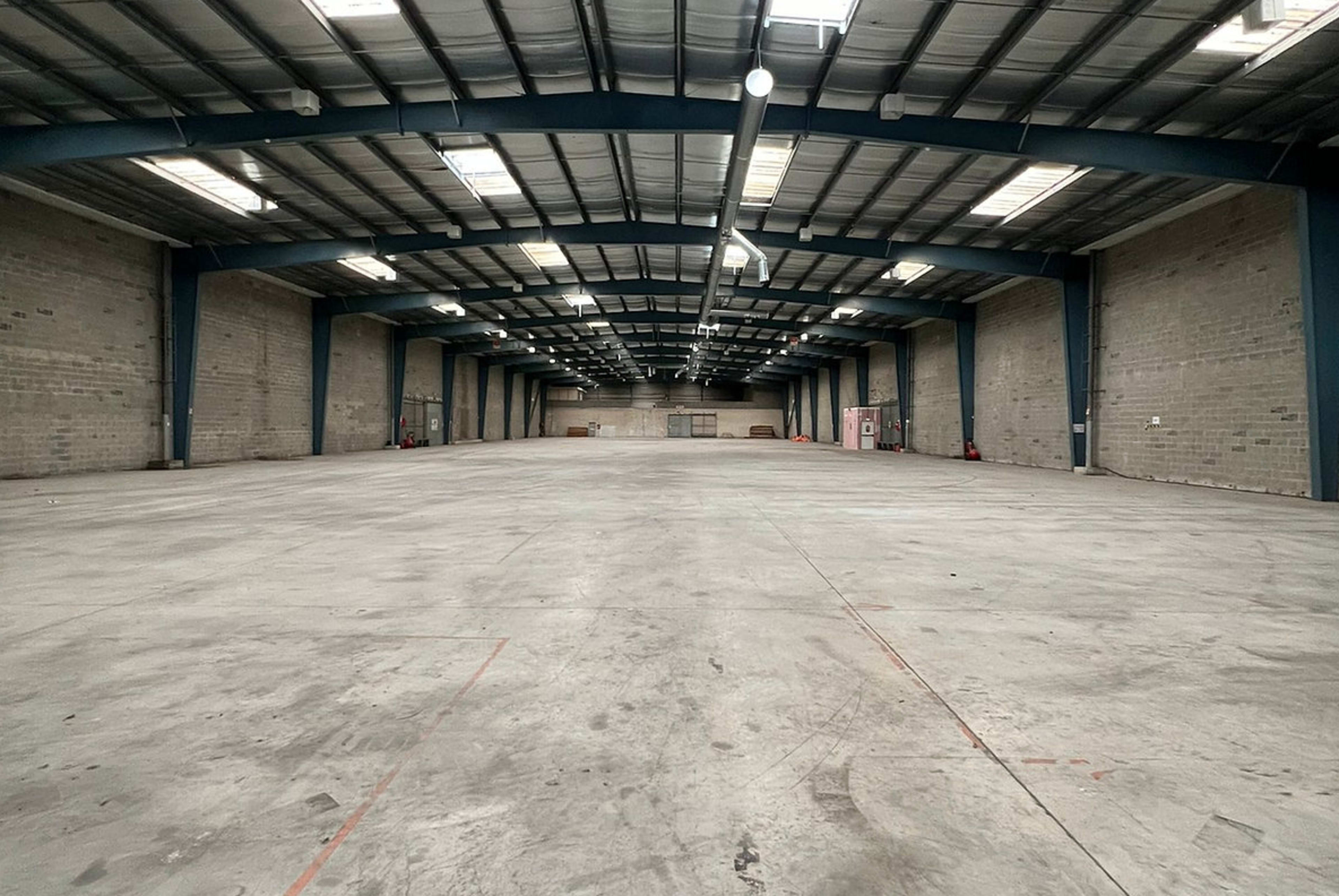 A large, empty industrial warehouse with concrete floors and high metal ceilings.
