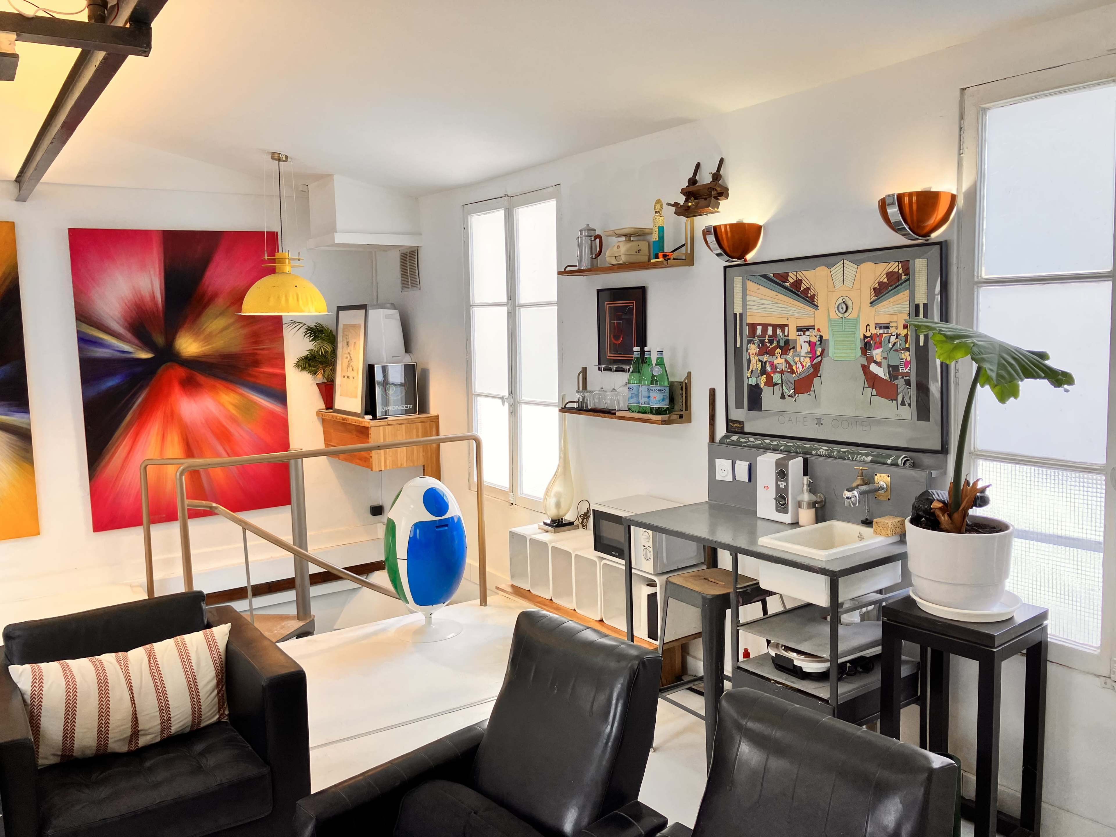 A modern living space with colorful artwork, a yellow pendant light, and a stylish seating area featuring black chairs and a decorative plant.