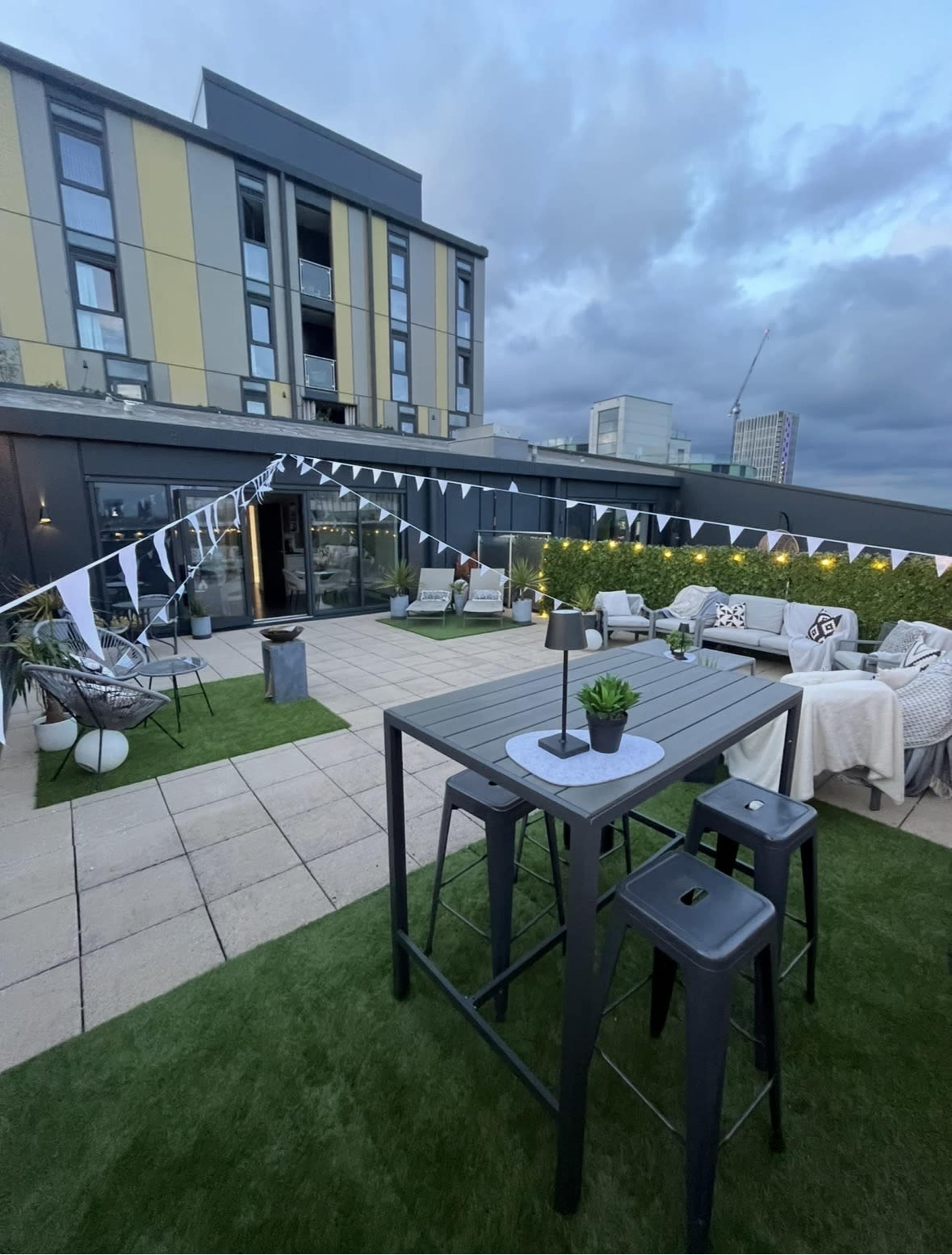 A rooftop terrace features a modern outdoor seating area, decorated with party bunting and surrounded by greenery.
