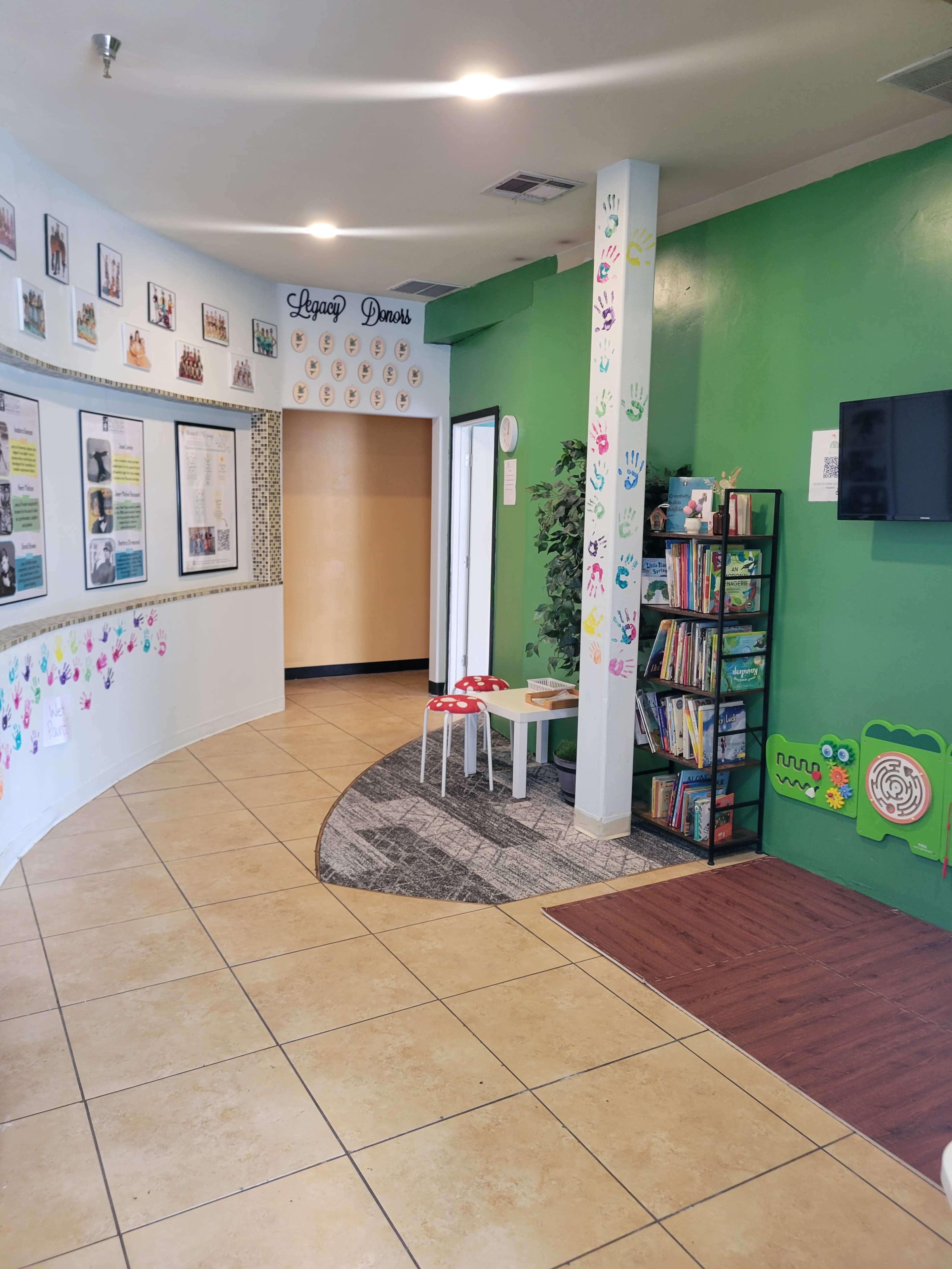 The image shows a brightly colored children's room with handprints on the walls, a bookshelf filled with books, and an inviting seating area.