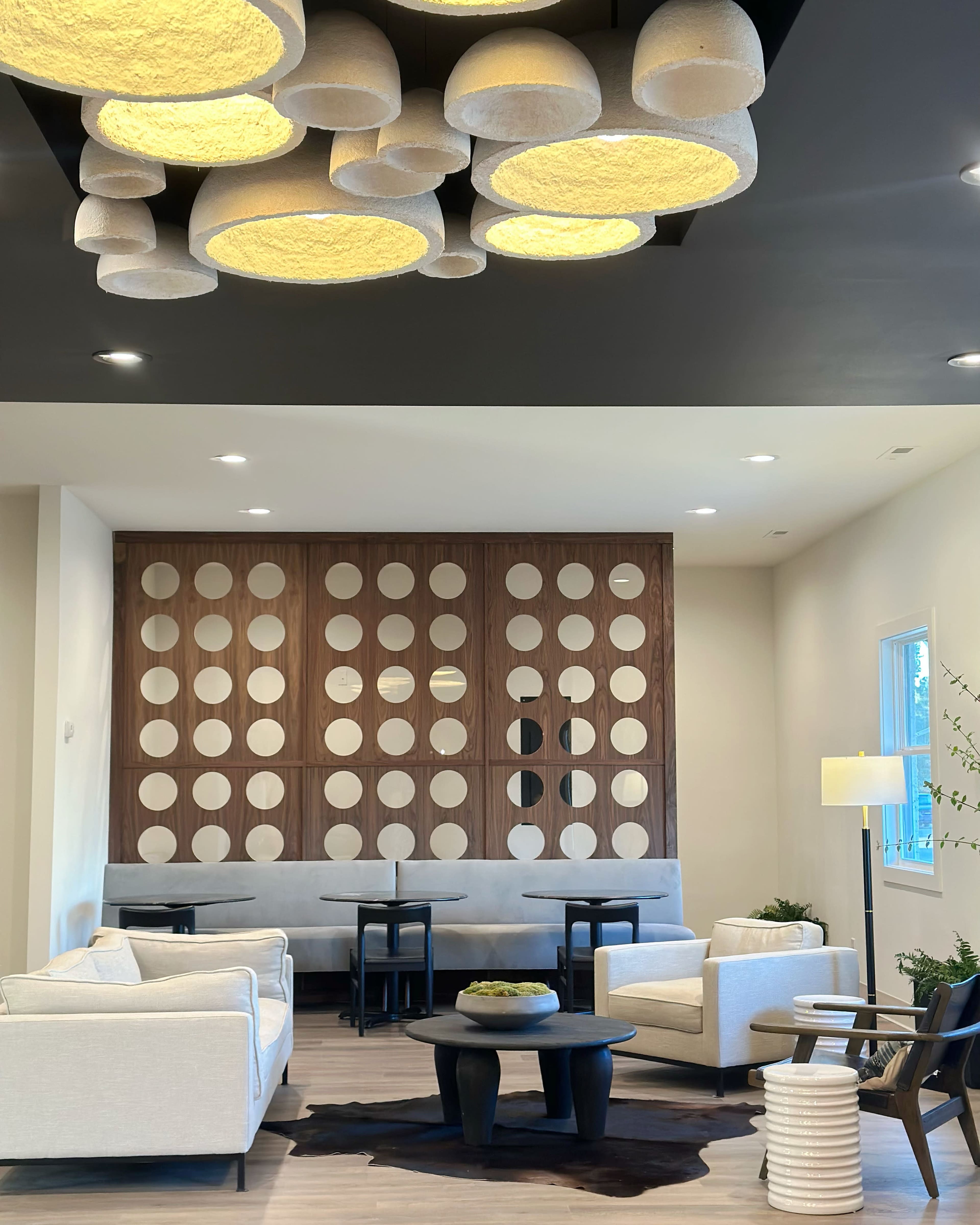 A modern lounge area with white couches, round tables, and a decorative wall featuring circular cutouts.