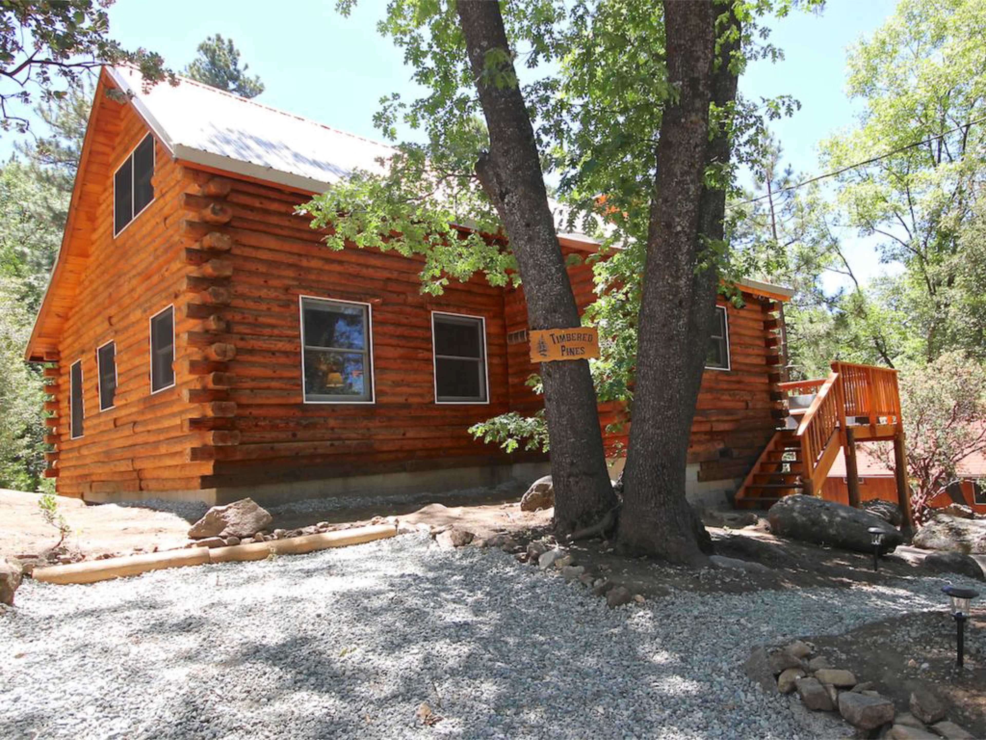 A log cabin with a metal roof is situated among trees and gravel pathways.
