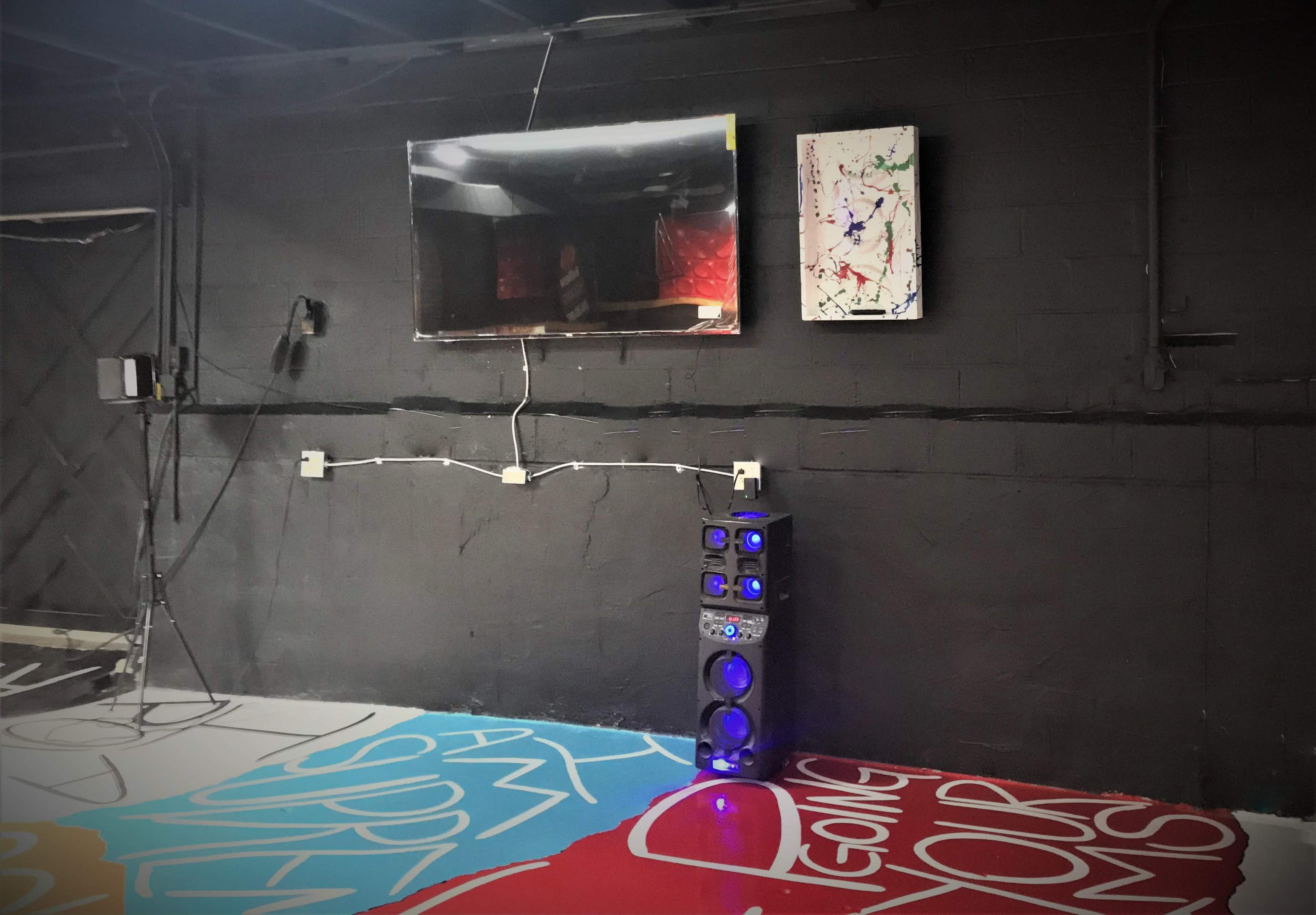A room with a black wall featuring a mounted television, a colorful abstract painting, and a tall speaker system on the floor.