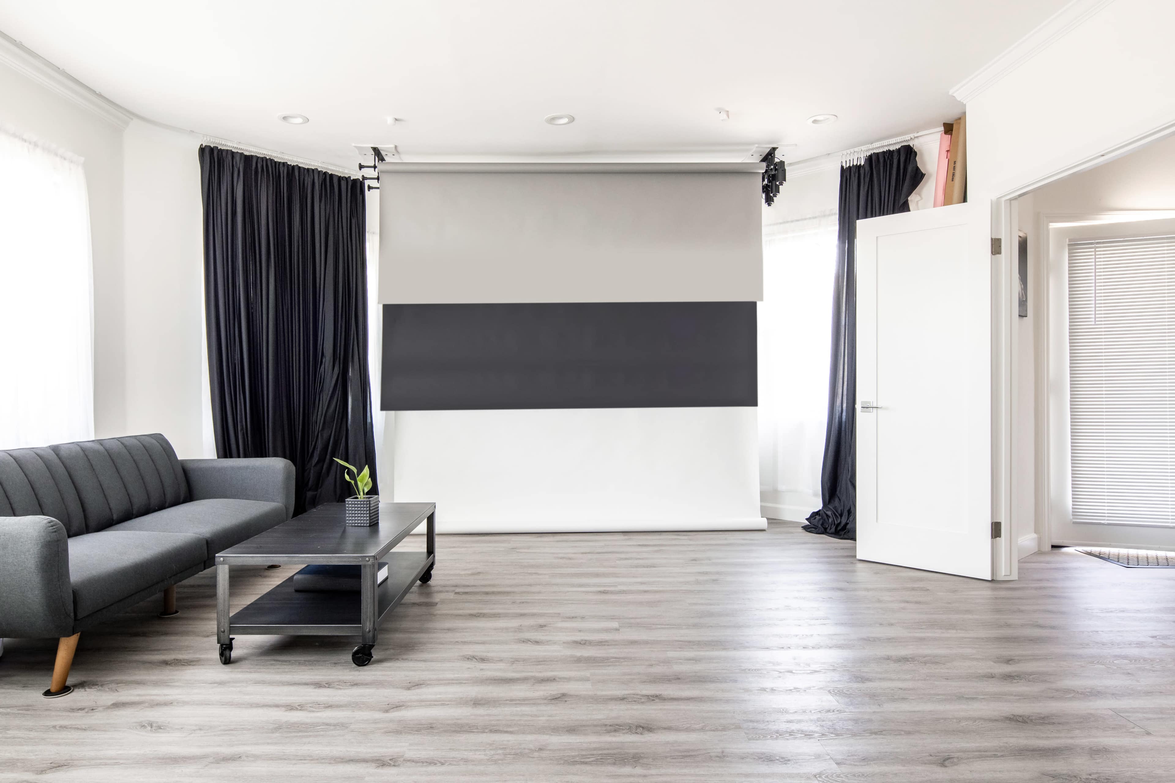 A modern living space featuring a gray sofa, a coffee table on wheels, and a photography backdrop setup with black and white panels.