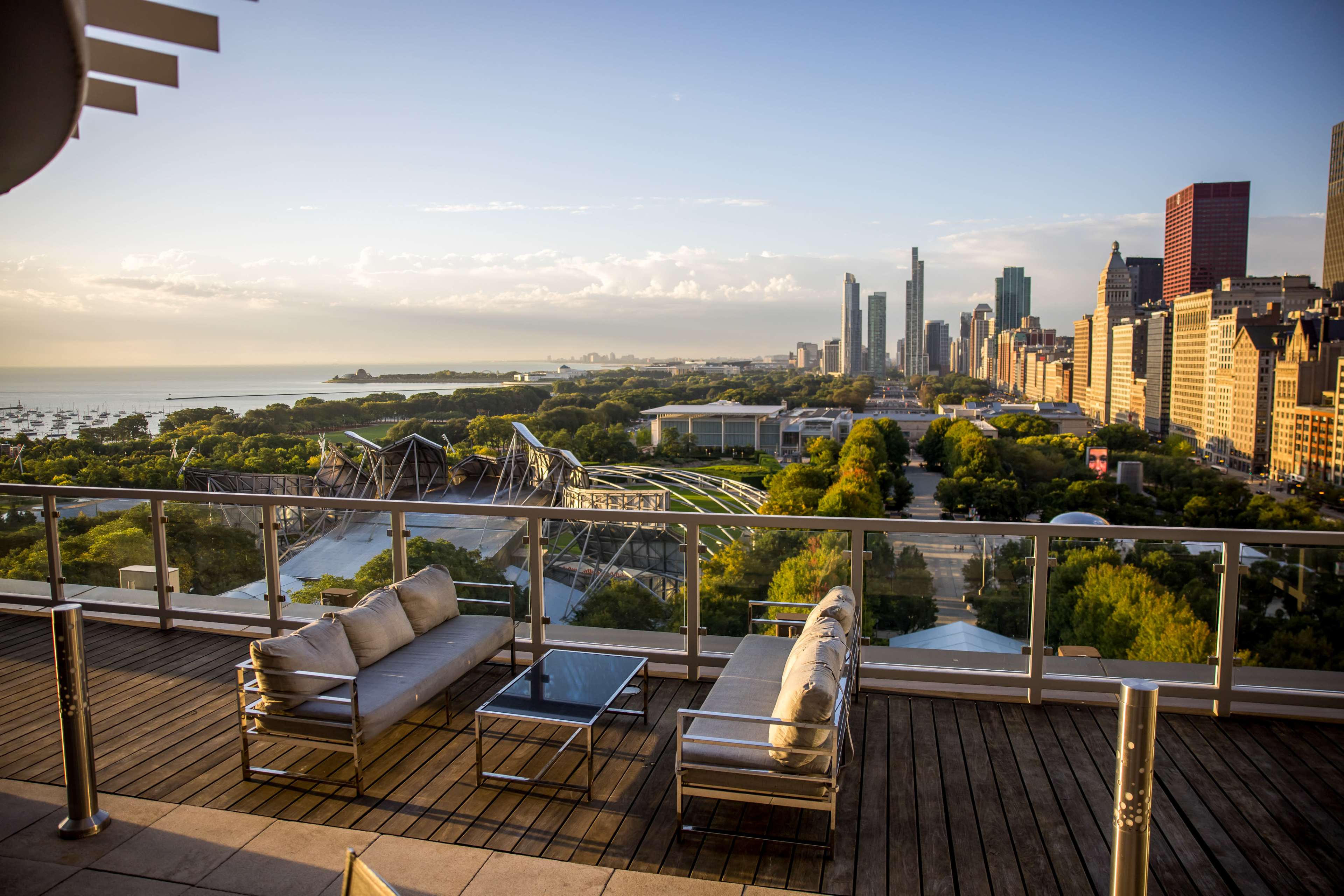 A rooftop view overlooking a city skyline with modern buildings, a park, and Lake Michigan in the distance.
