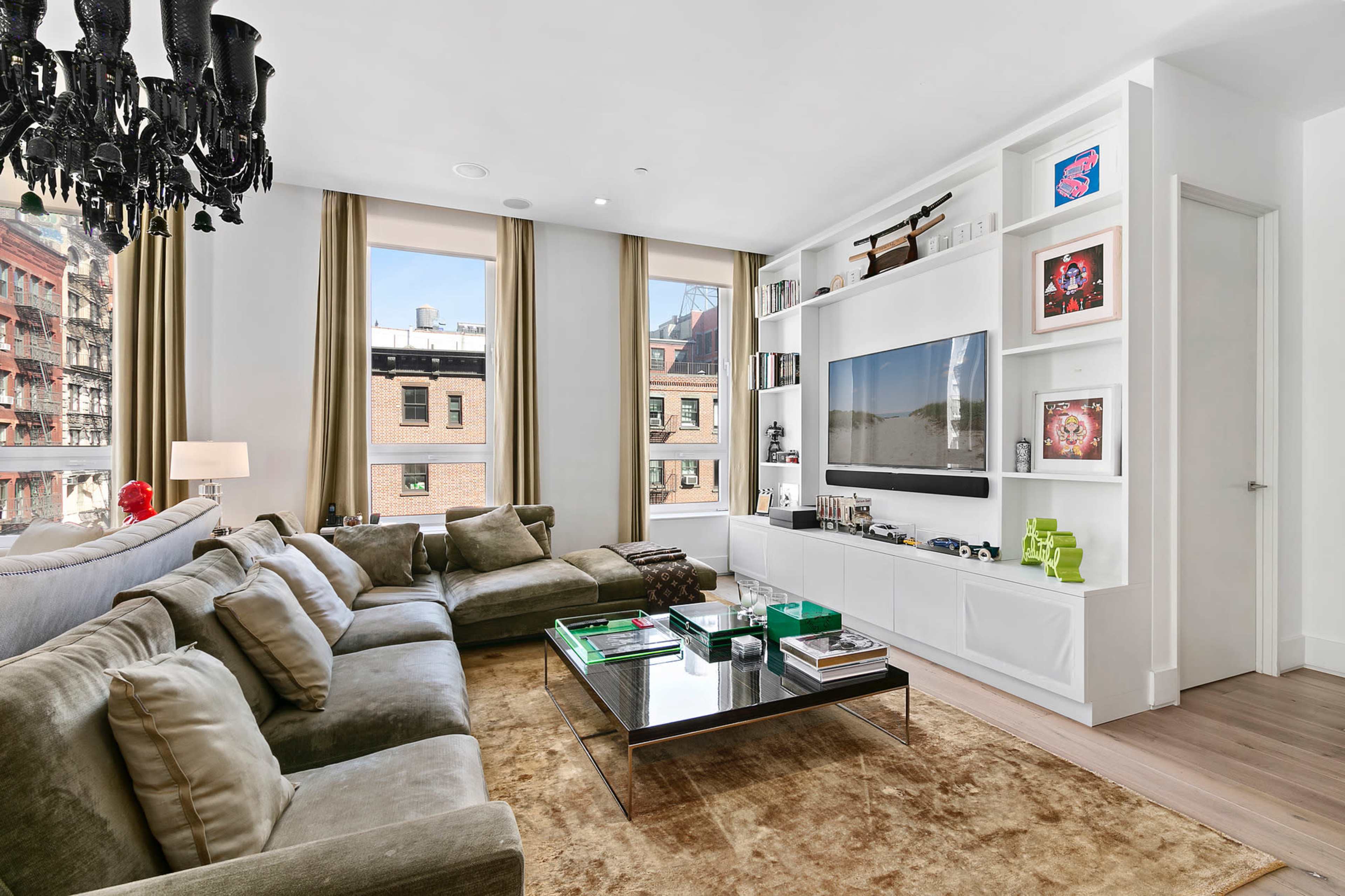 A modern living room features a large sectional sofa, a glass coffee table, and a media console against a wall of windows.