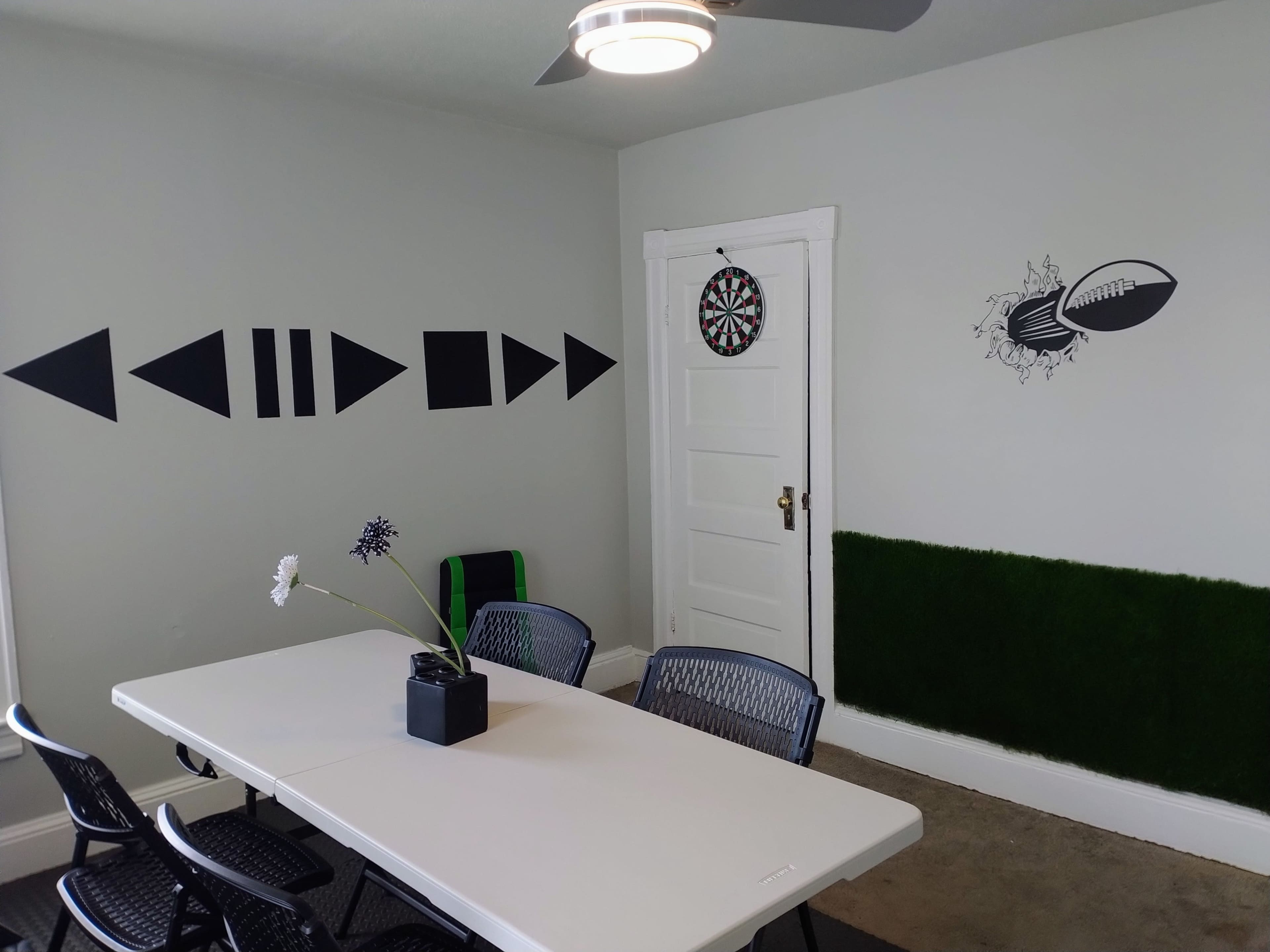A meeting room with a white table surrounded by black chairs, featuring wall decorations of geometric shapes and a dartboard.