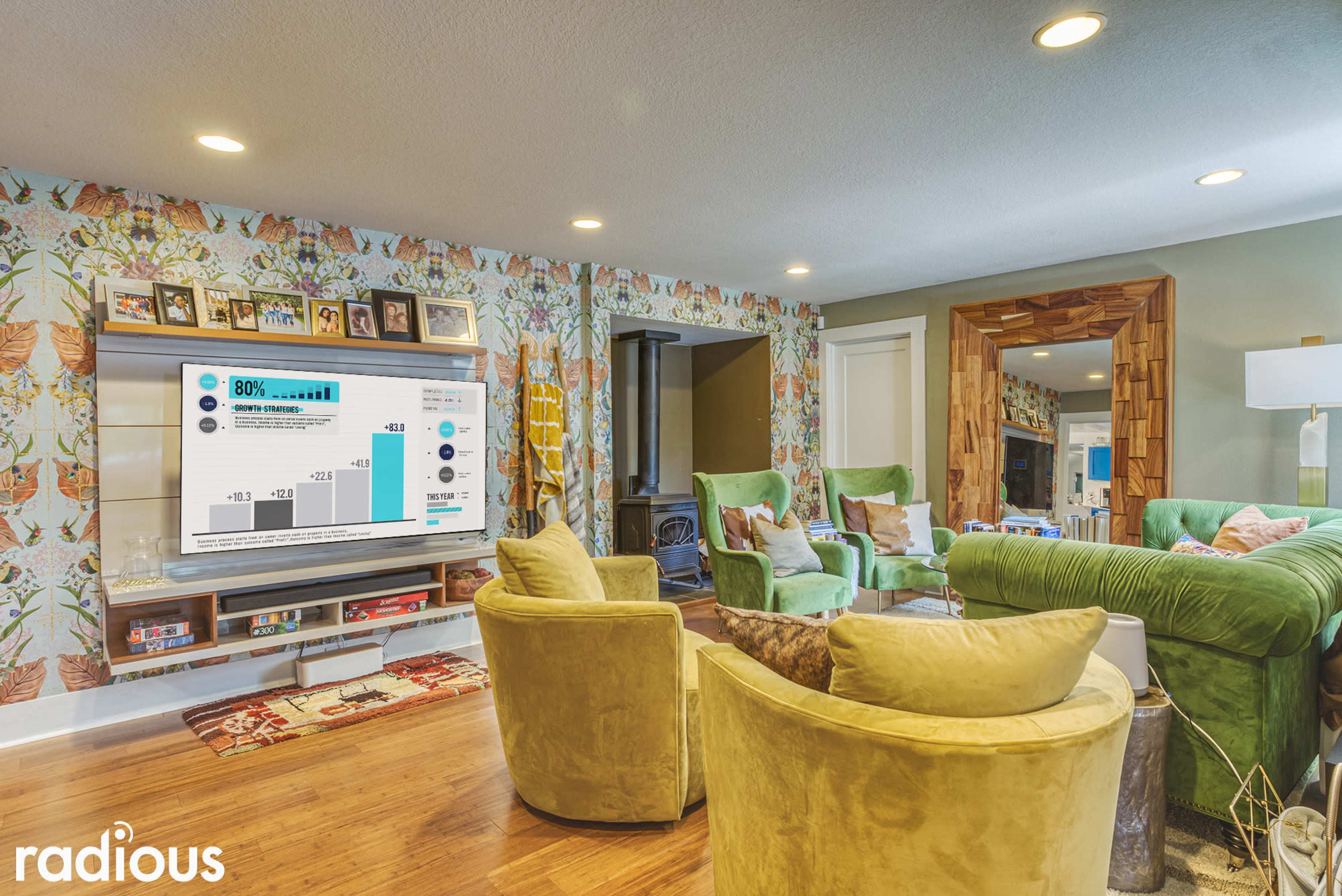 A modern living room features a TV mounted on a wall with floral wallpaper, surrounded by green armchairs and a sectional couch.