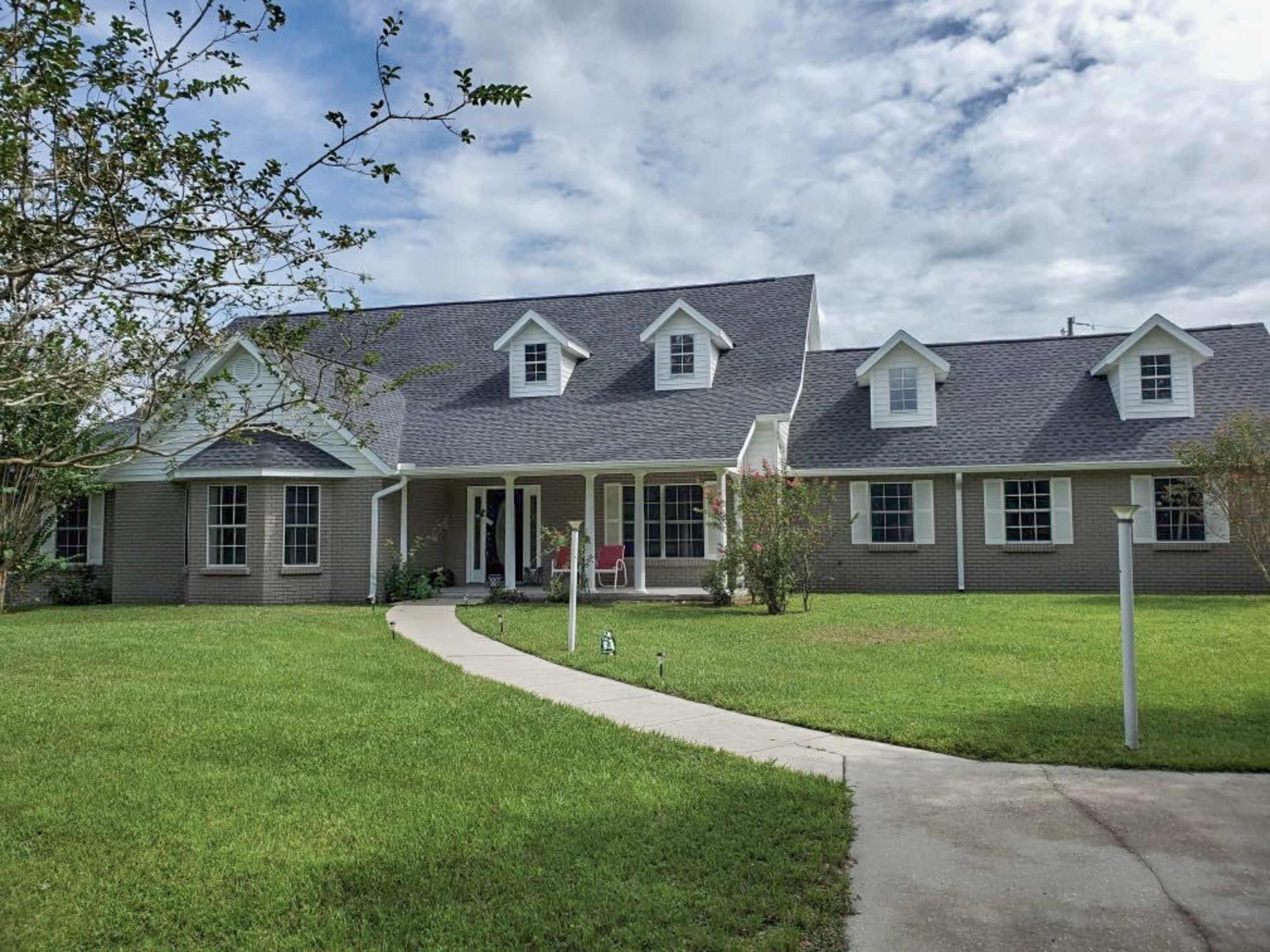 A large, two-story house with a gray roof and porch sits on a well-maintained lawn.
