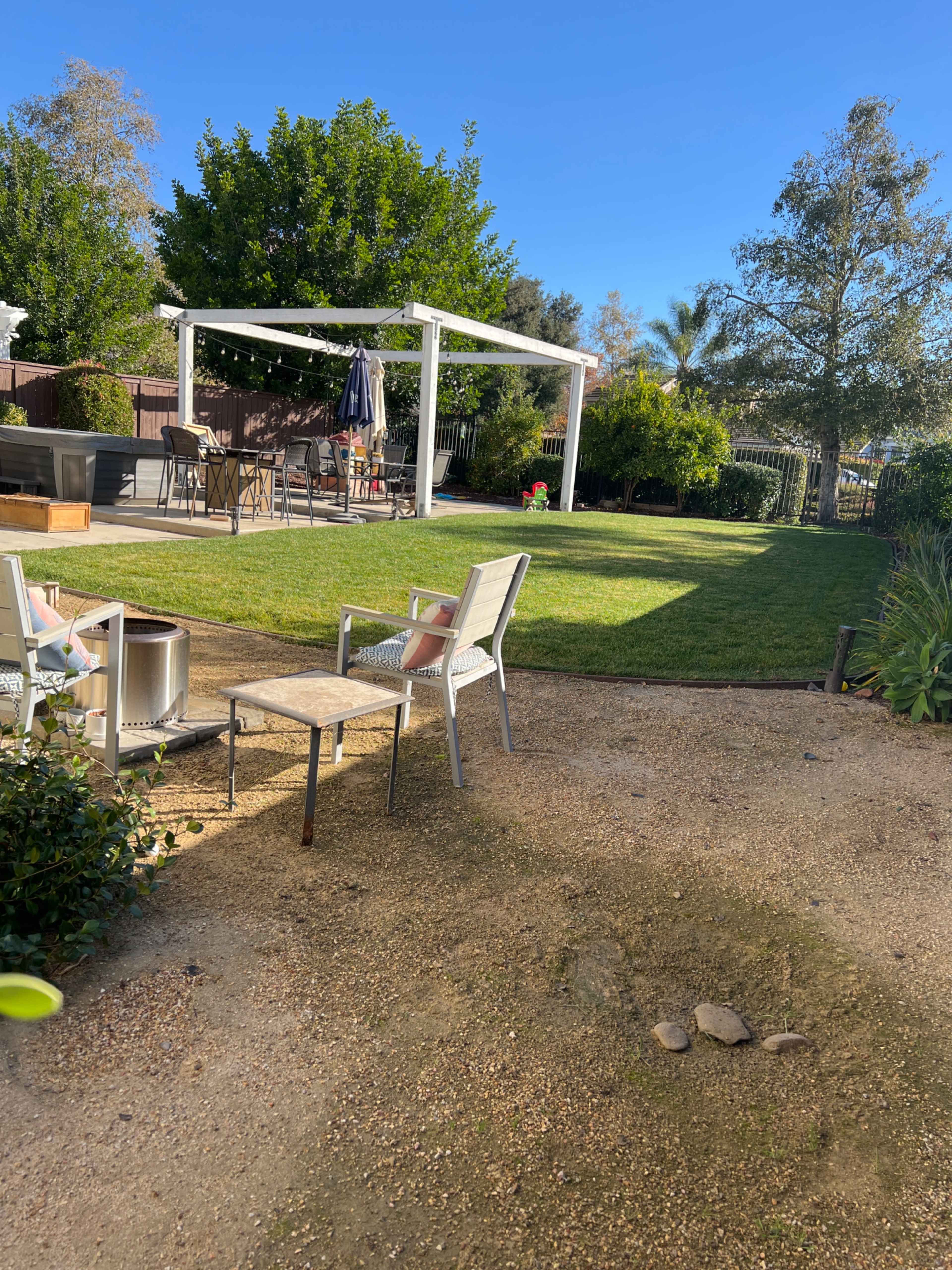 The image shows a landscaped backyard featuring a grassy area, patio furniture, and a pergola.