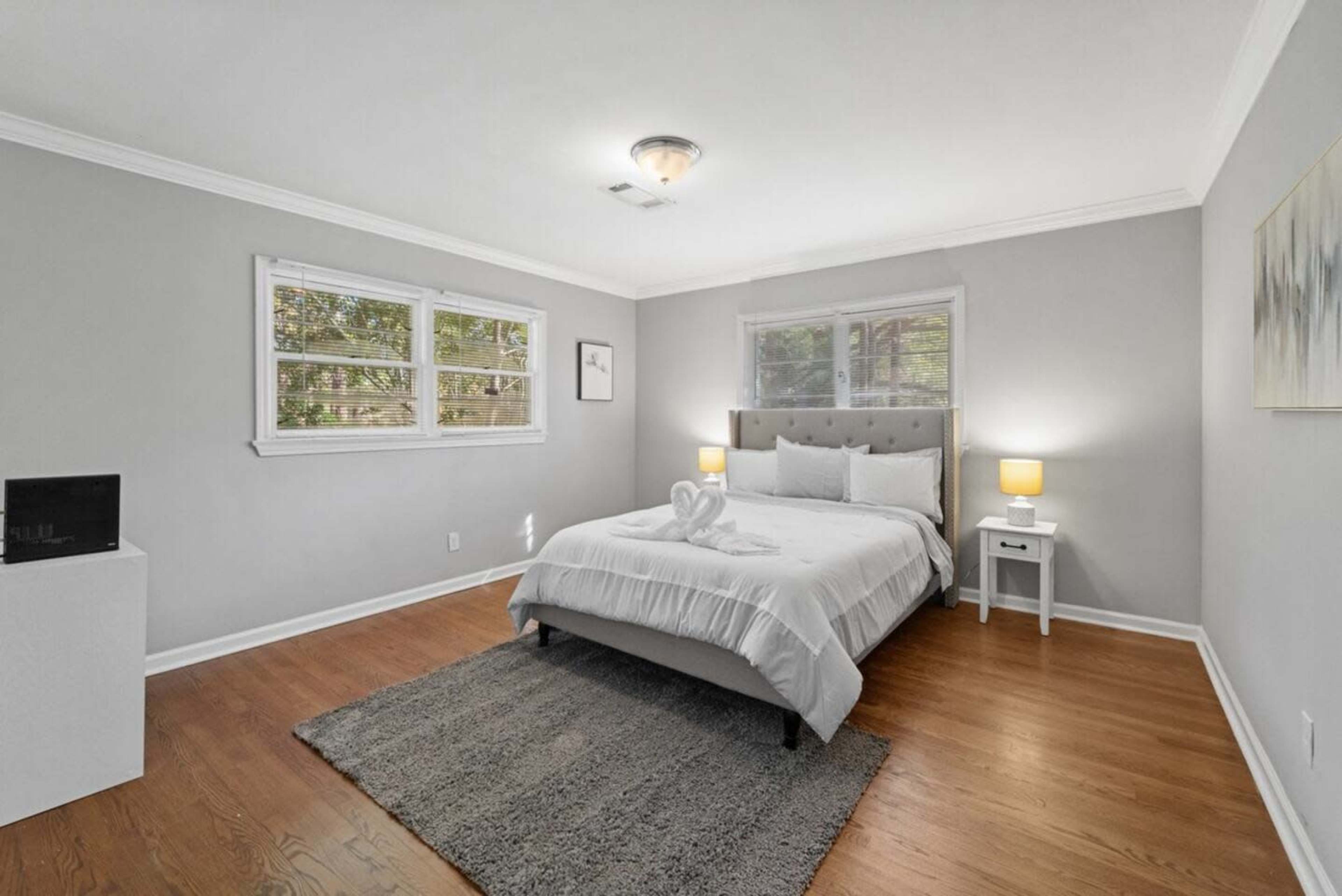 The image shows a neatly arranged bedroom with a queen-sized bed, a light-colored rug, and two bedside lamps.