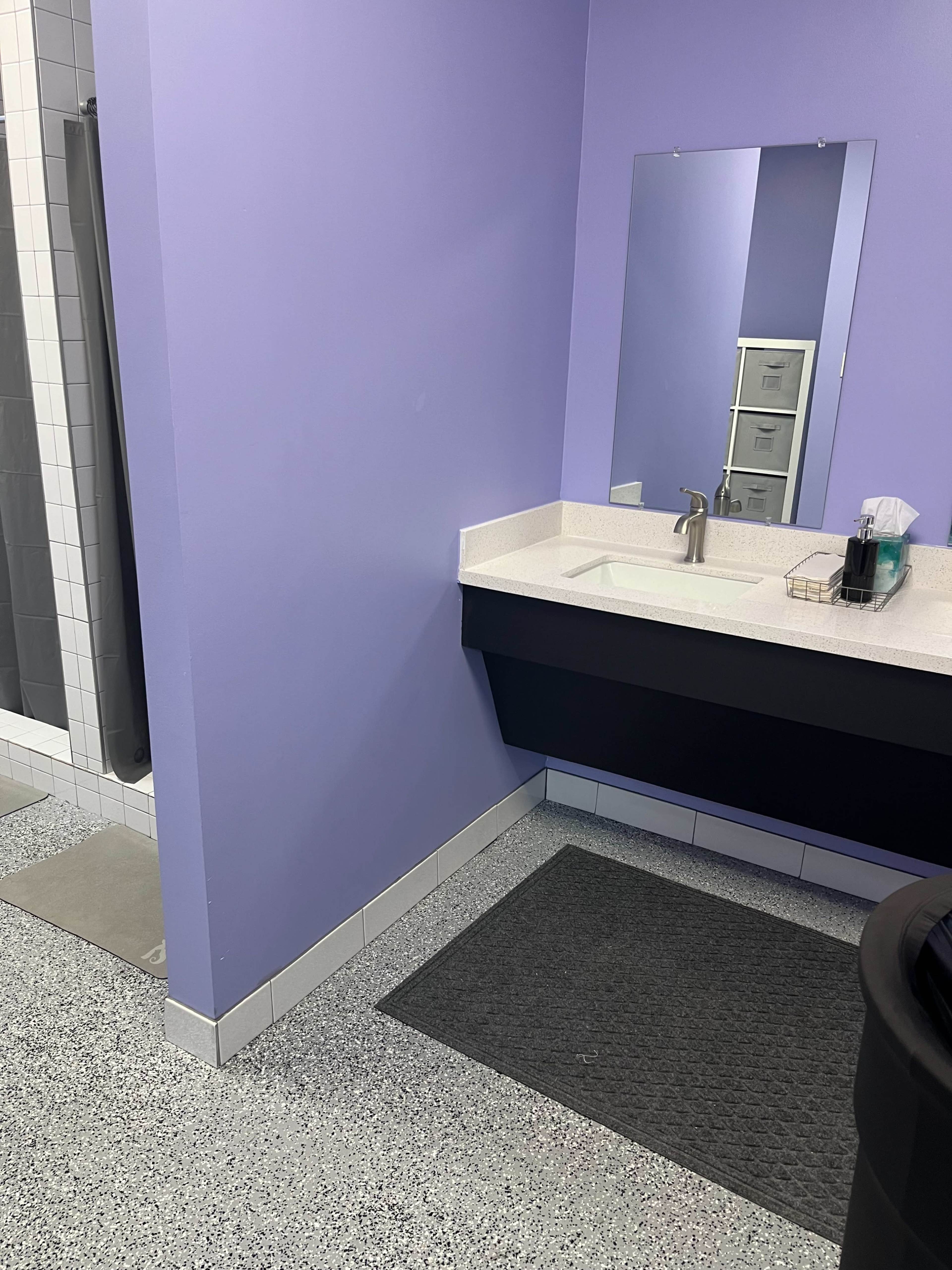 The image shows a bathroom with a purple wall, a sink with a faucet, and a shower area partially visible behind a curtain.