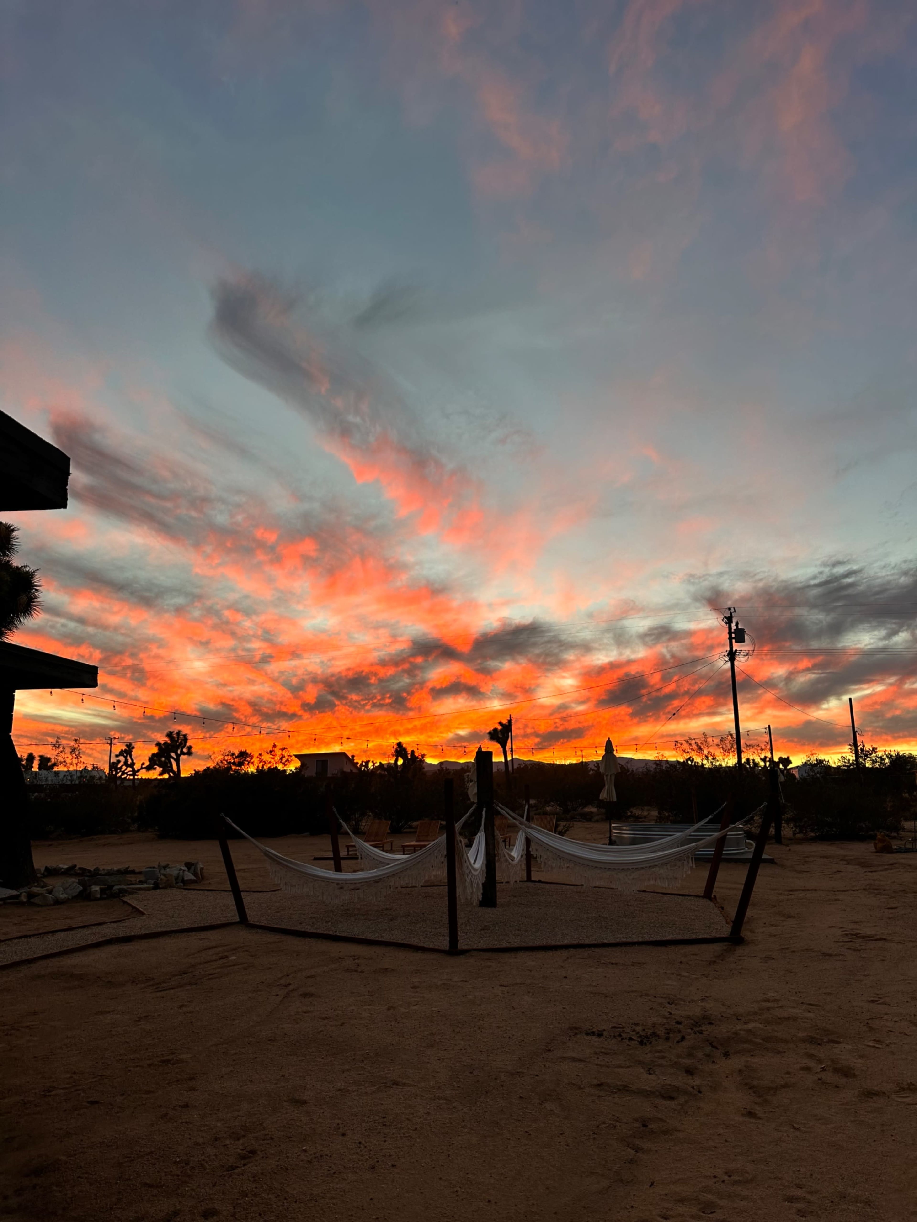 The scene shows a desert landscape at sunset with colorful clouds and two hammocks set up near a sandy area.