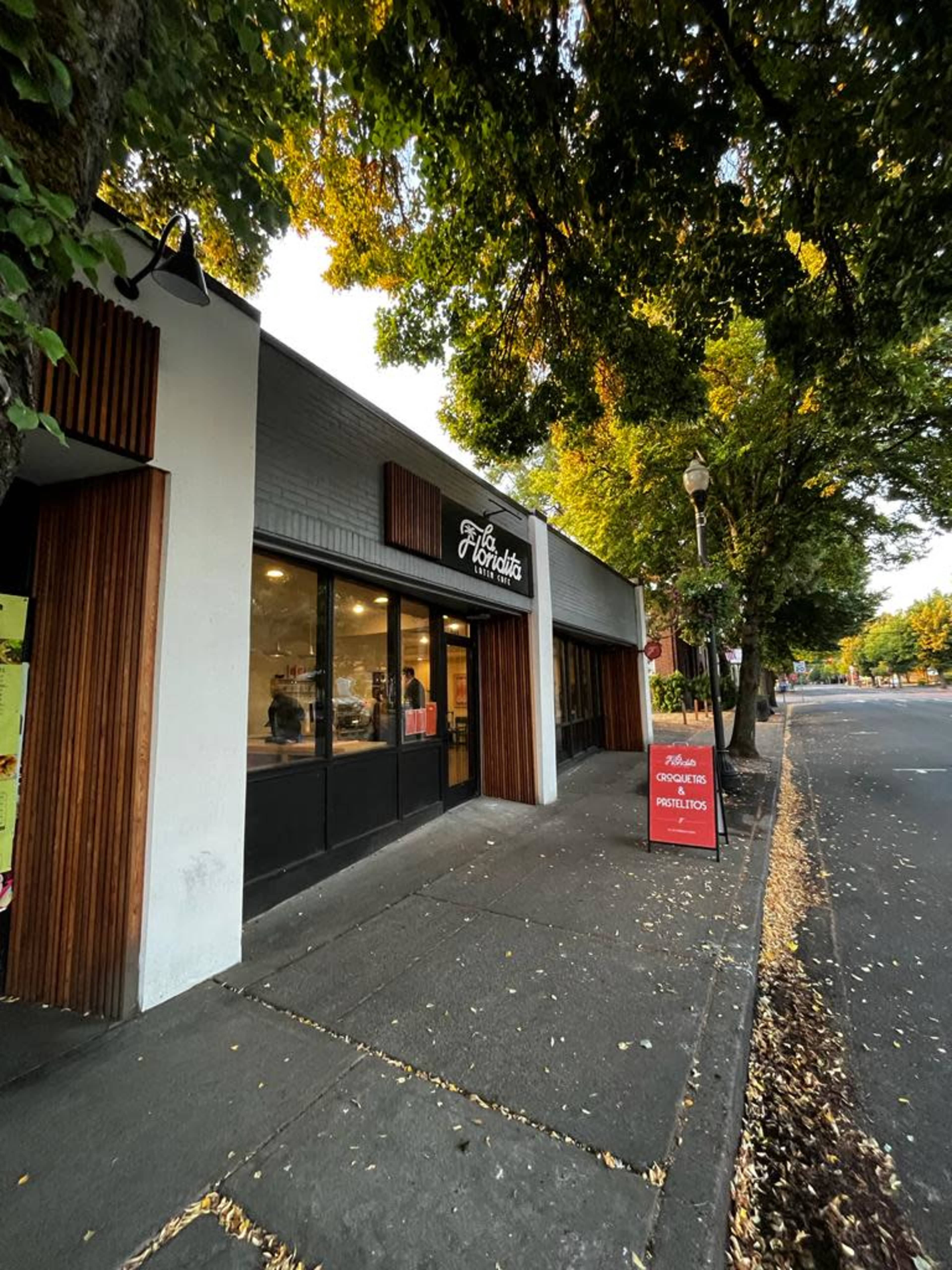 A storefront with a sign that reads "The Horditis," located on a sidewalk lined with trees.