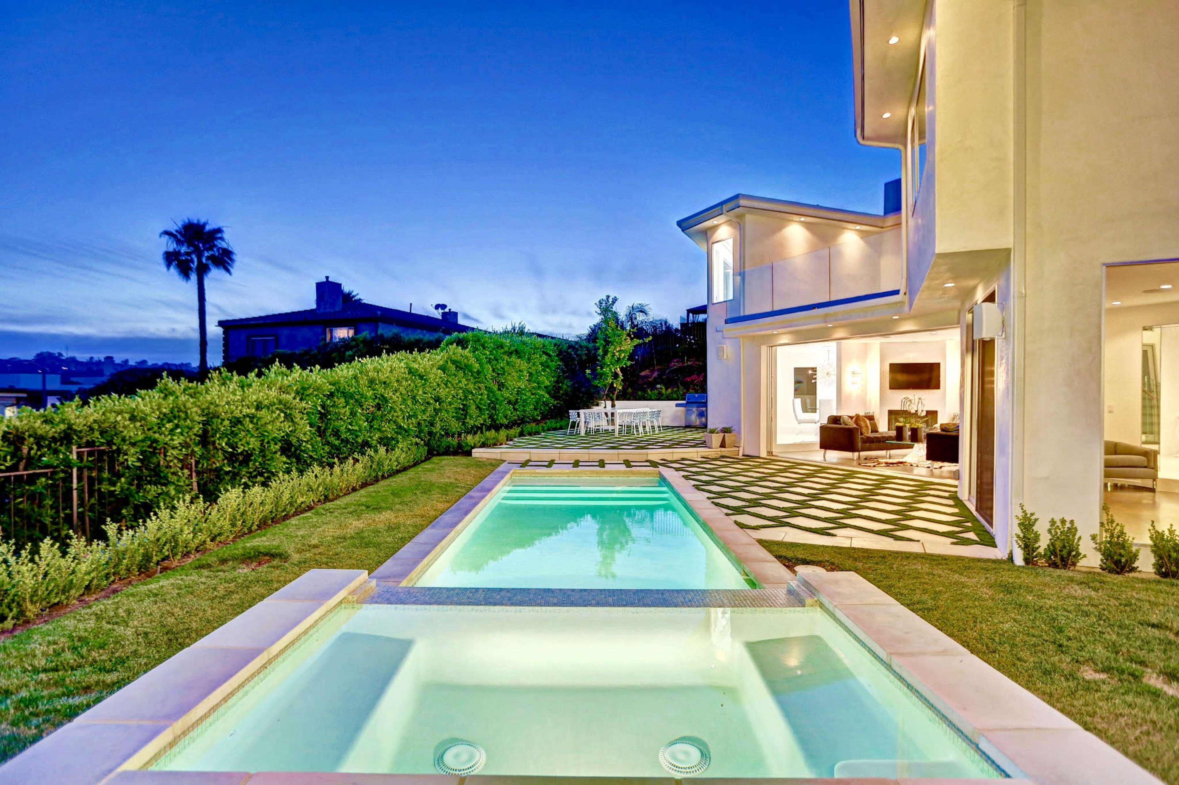 A modern house with a pool in the foreground and a landscaped yard, under a twilight sky.