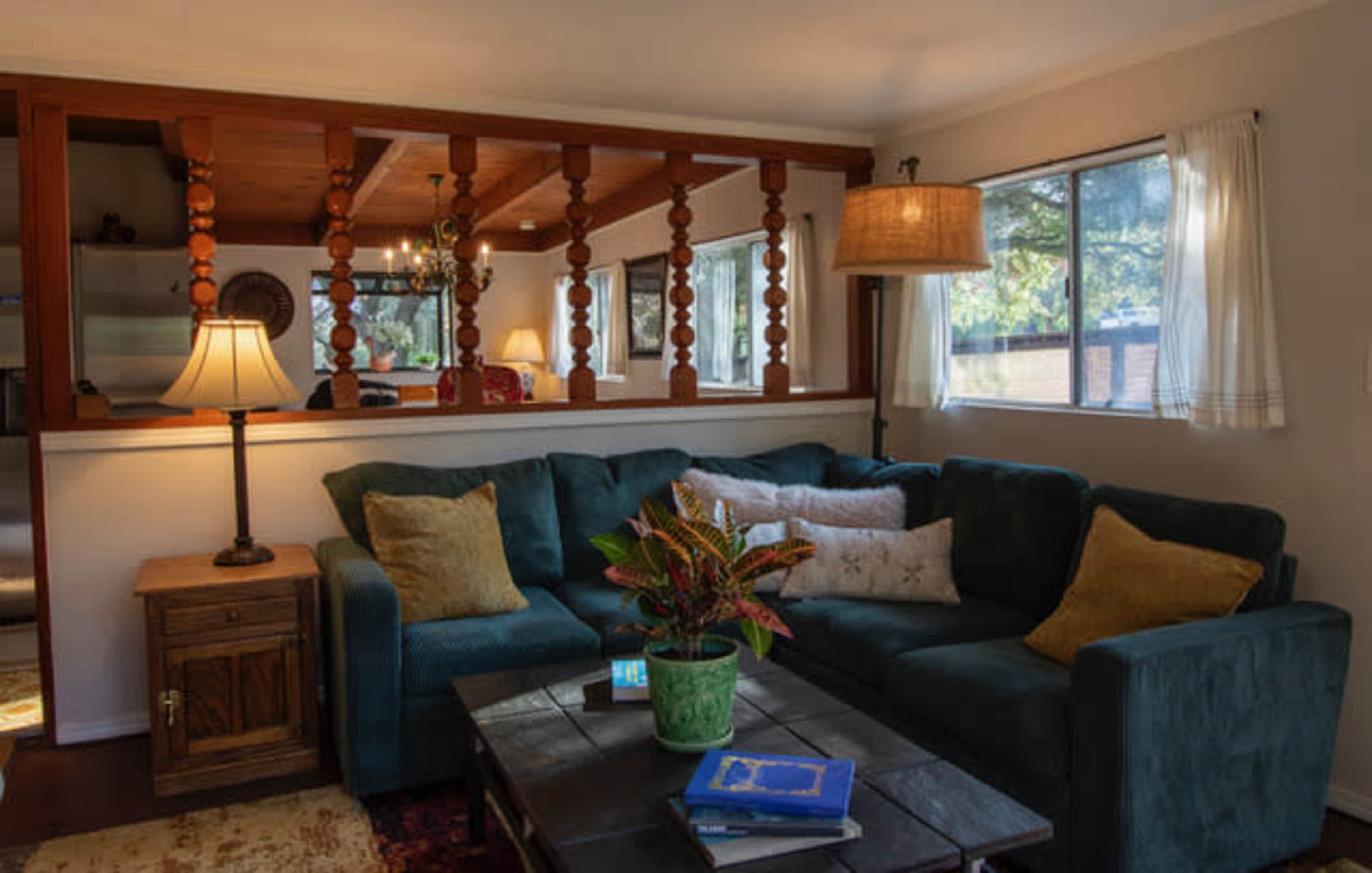 A cozy living room features a green sectional sofa, a wooden coffee table, and a potted plant, with a light fixture illuminating the space.