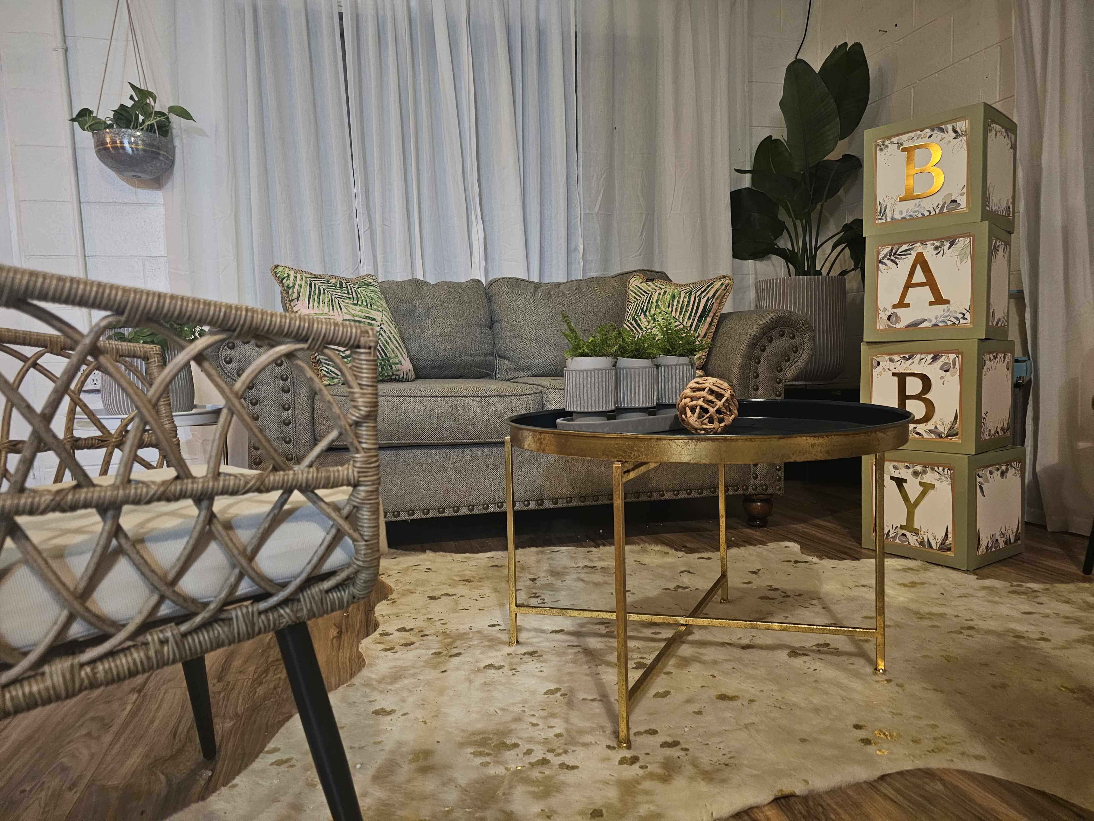 A cozy living room setup with a grey couch, a round coffee table, decorative boxes labeled "BABY," and a textured rug.