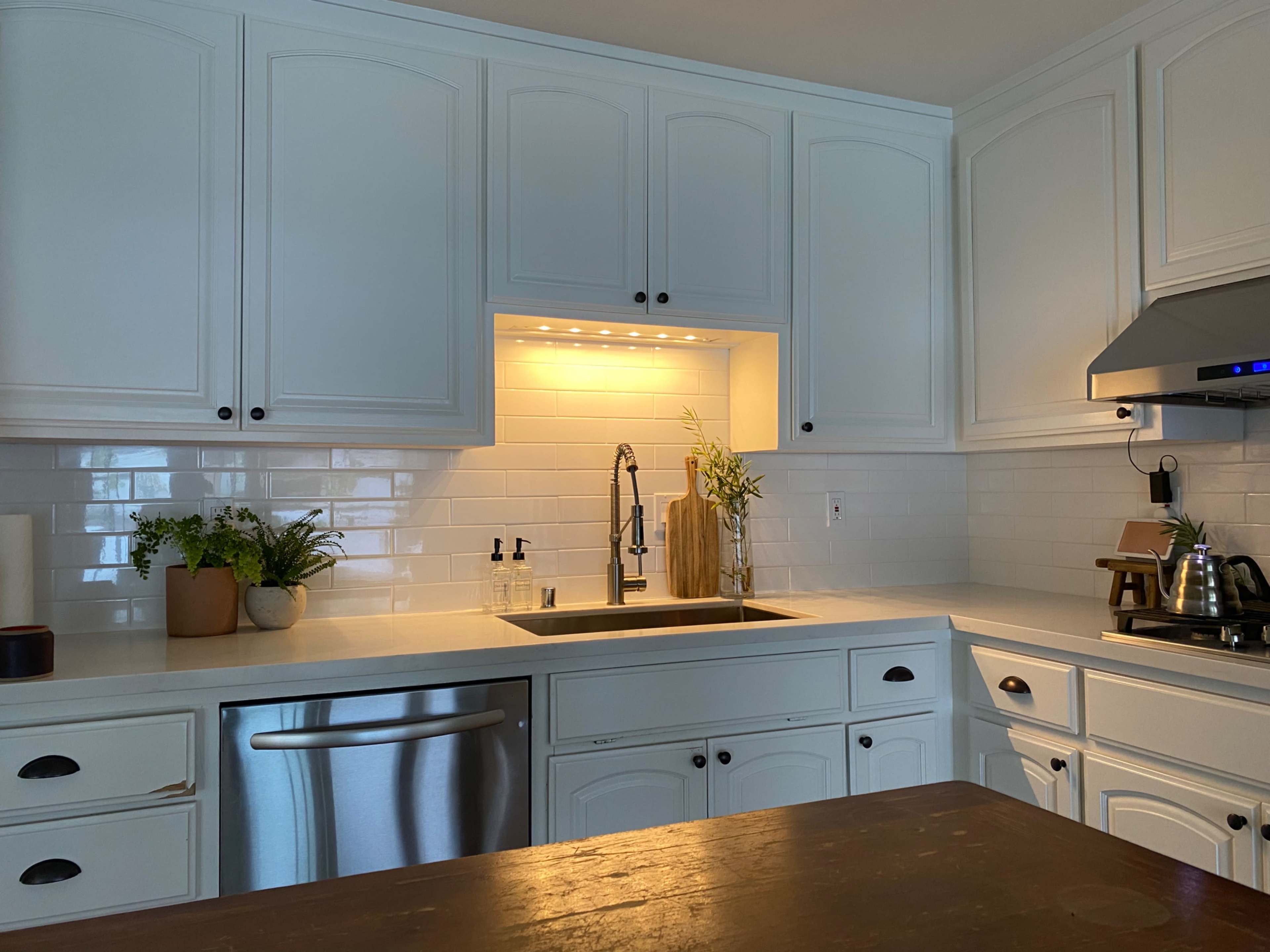 A modern kitchen features white cabinetry, a stainless steel sink, and a backsplash of white subway tiles.