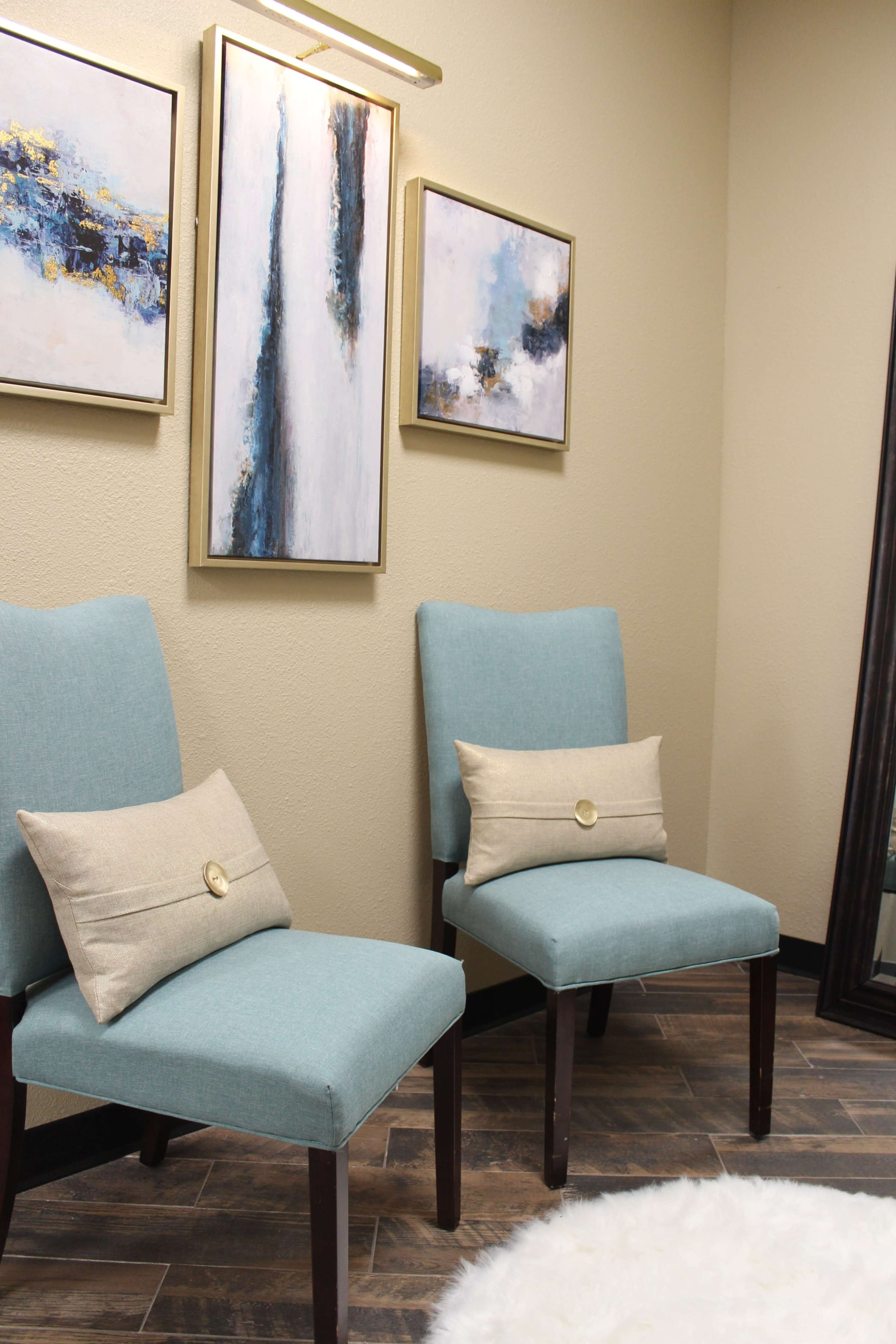 Two blue upholstered chairs with decorative pillows positioned against a wall decorated with framed abstract artwork.