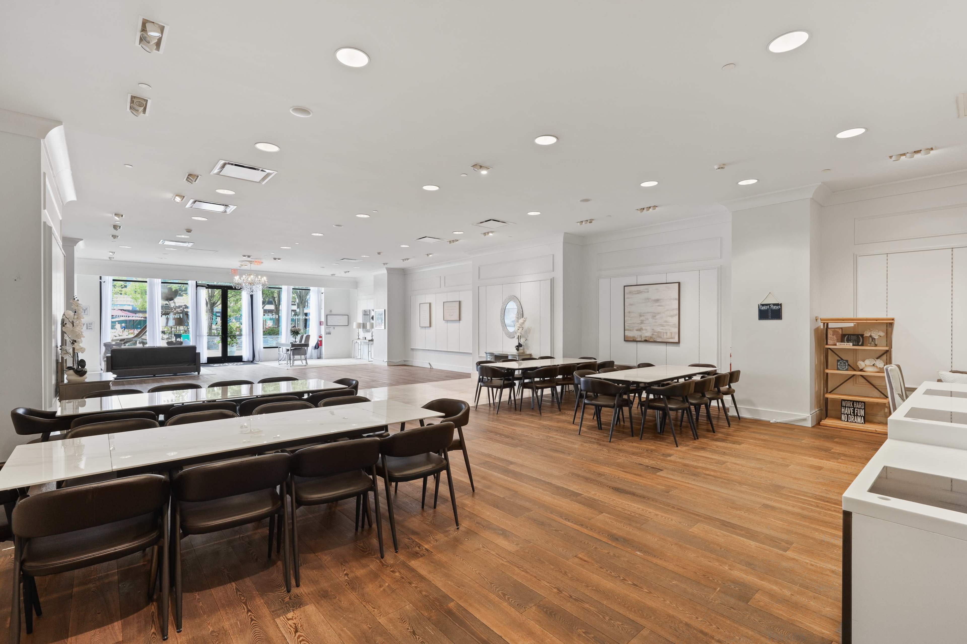 The image shows a spacious, modern interior with wooden flooring, multiple tables and chairs arranged for seating, and bright overhead lights.